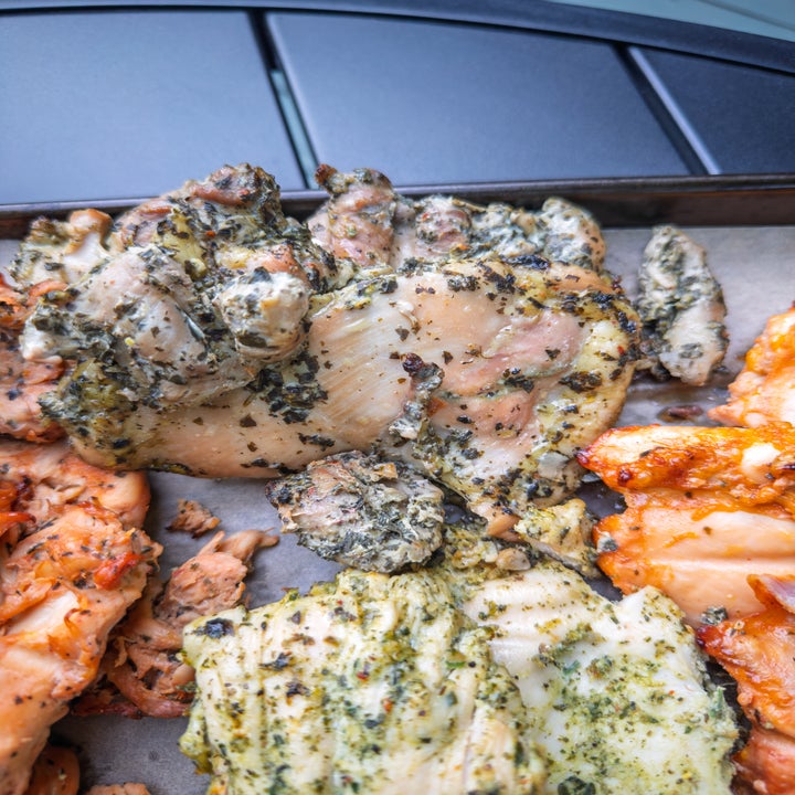 Assorted grilled chicken pieces with herbs and seasonings on a baking sheet
