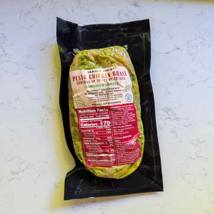 Packaged Trader Joe's pesto chicken breast on a marble-like surface, showcasing nutrition facts and ingredients