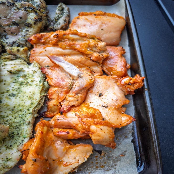 Grilled chicken pieces on a baking tray, with visible herbs and spices
