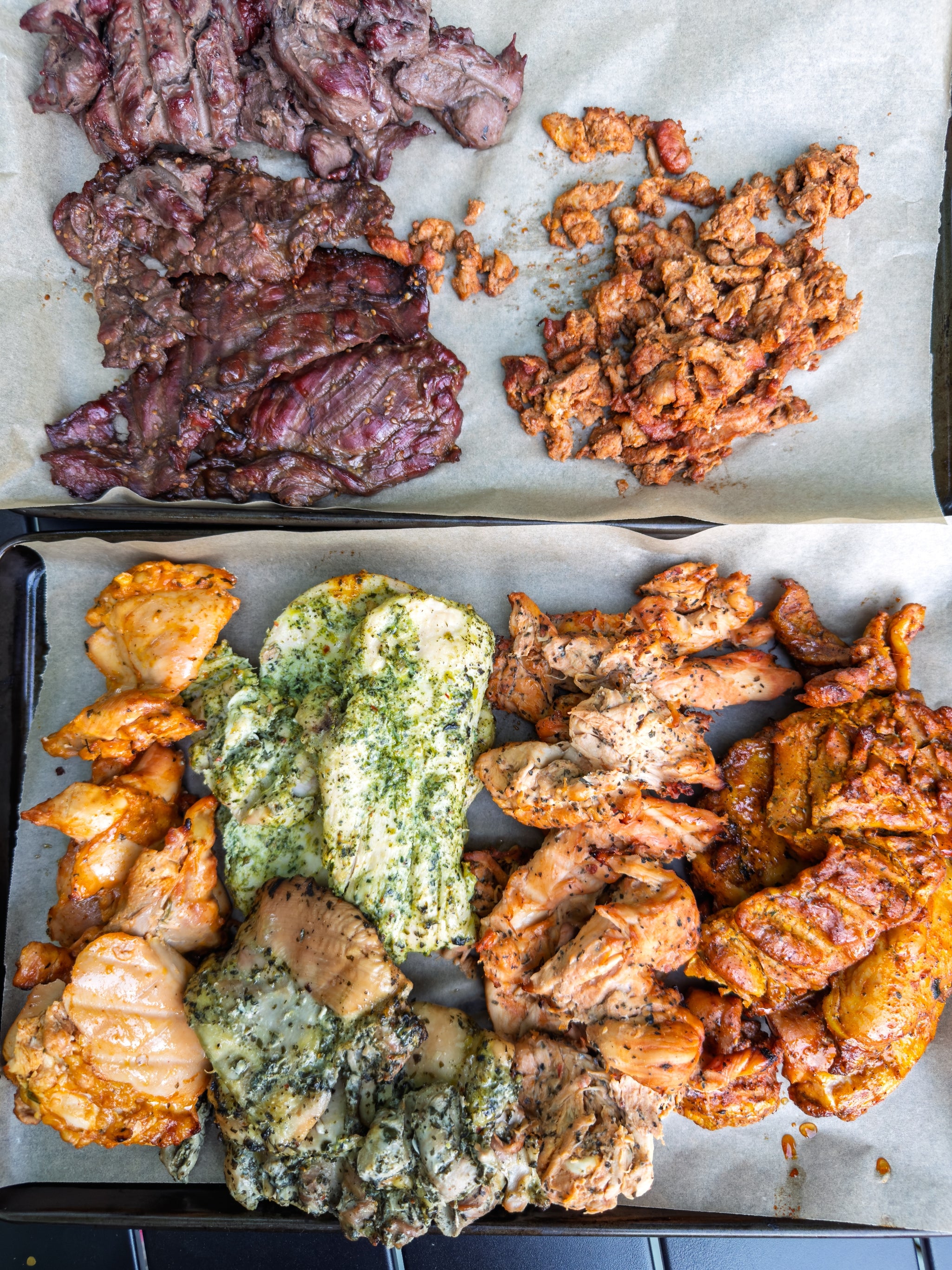 Various types of cooked meats arranged on parchment paper, including grilled steak, seasoned chicken, and marinated pork