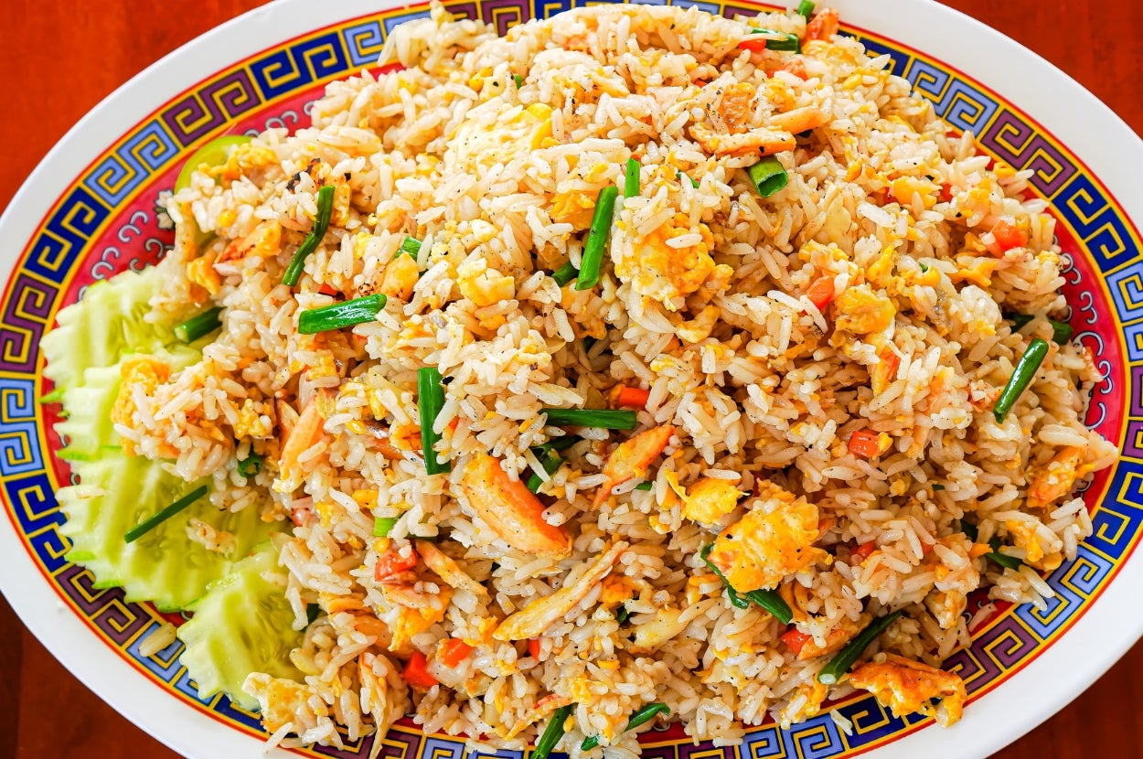 A plate of fried rice with vegetables and egg, garnished with green onions and sliced cucumbers
