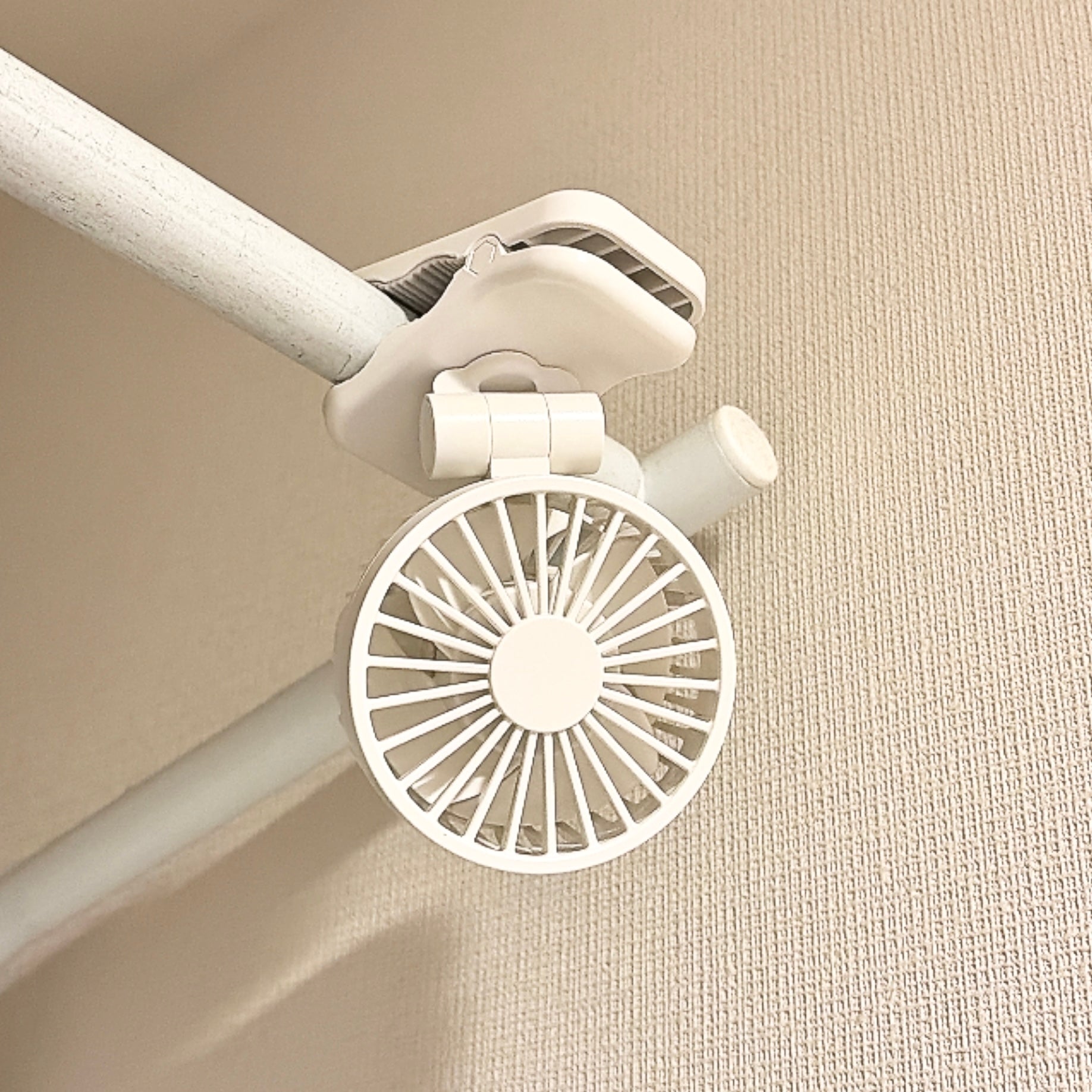 無印良品「置いても使える 充電式クリップファン ミニ」クランプでパイプに取り付けられた小型の白い扇風機。