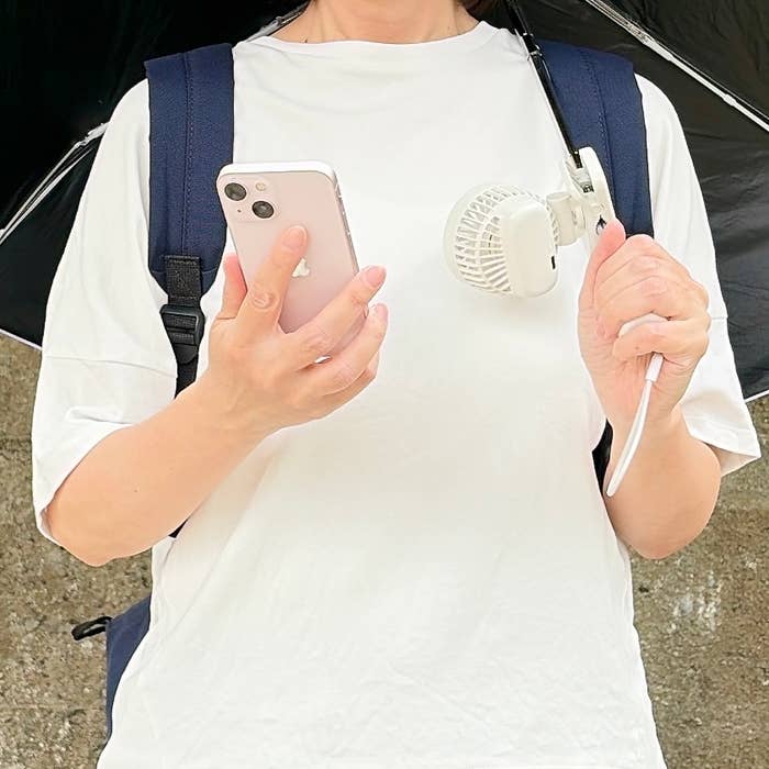 無印良品「置いても使える 充電式クリップファン ミニ」女性が白いTシャツを着て、携帯ファンを身につけ、スマートフォンを手に持っています。