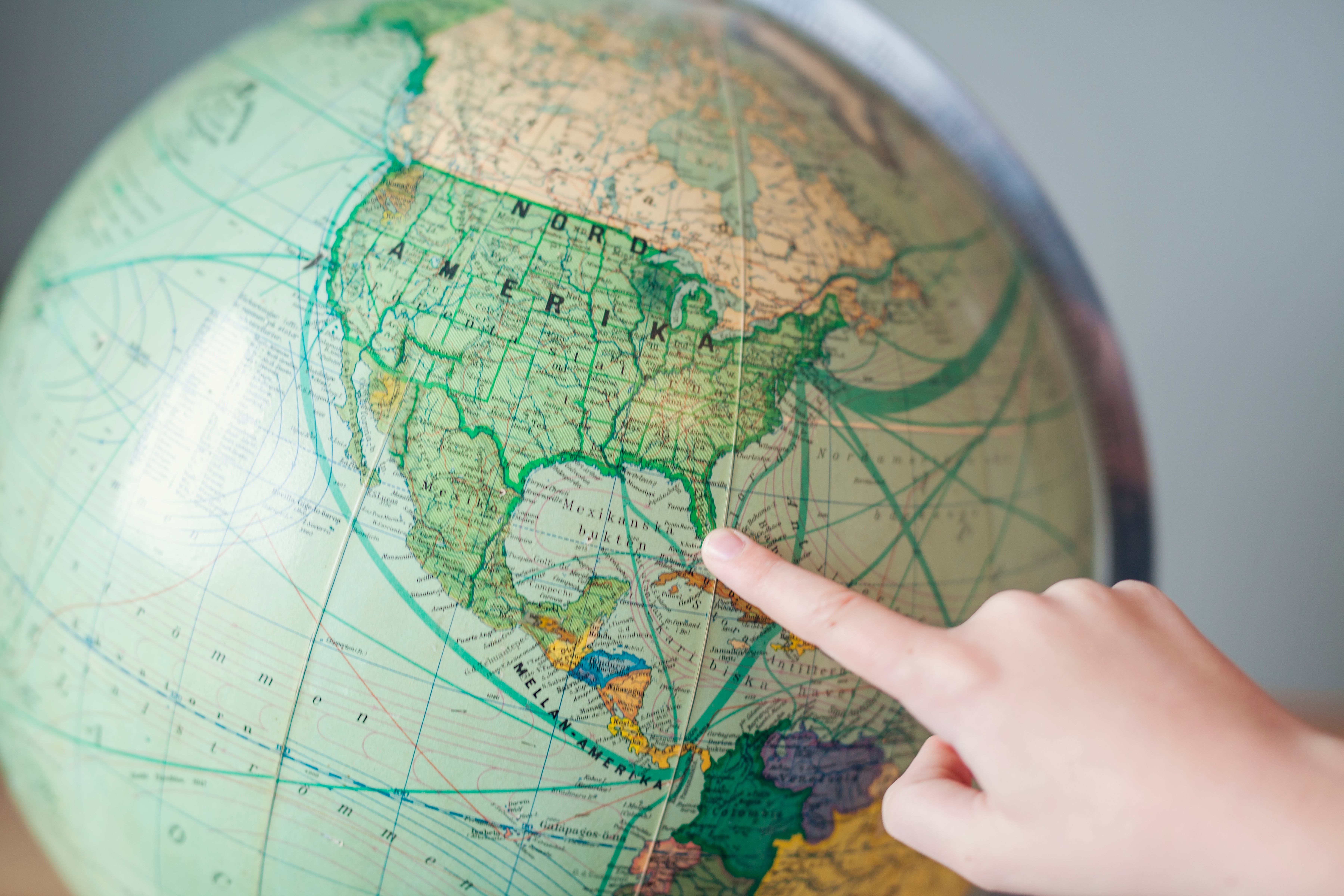 A hand points to a location on a globe, focusing on North America, suggesting exploration or travel in a gaming context