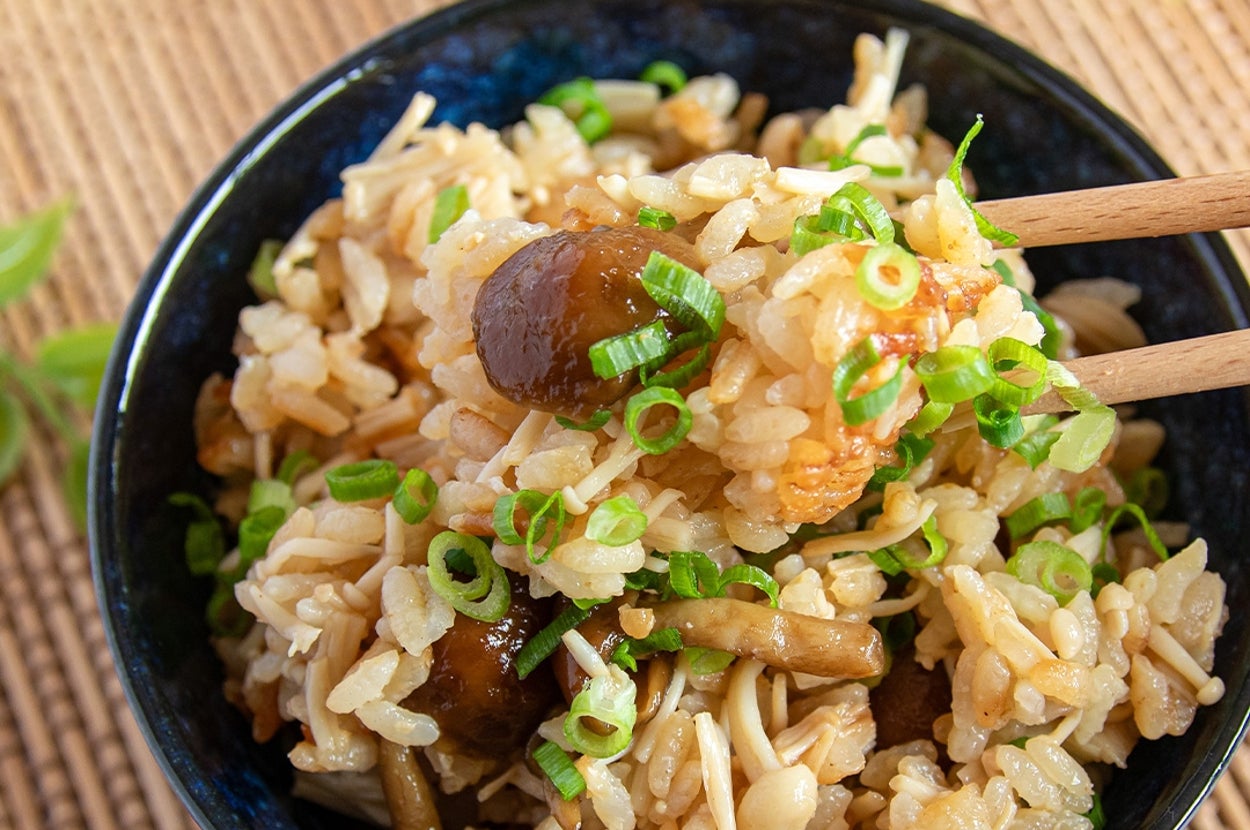 きのこご飯が盛られた黒い器。箸で一口分を持ち上げている。小ねぎがトッピングされている。