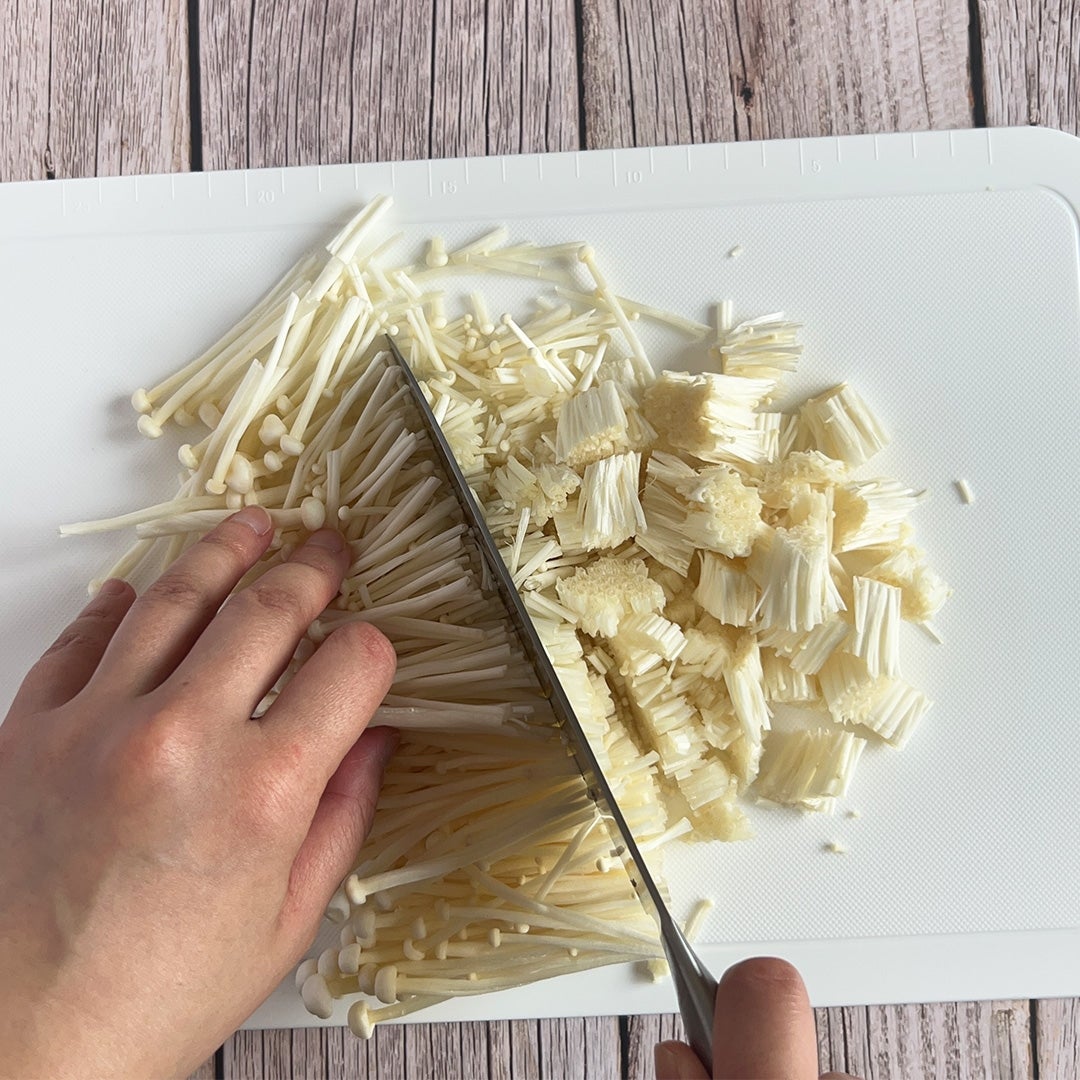 まな板の上でえのきを包丁で切っている手元。