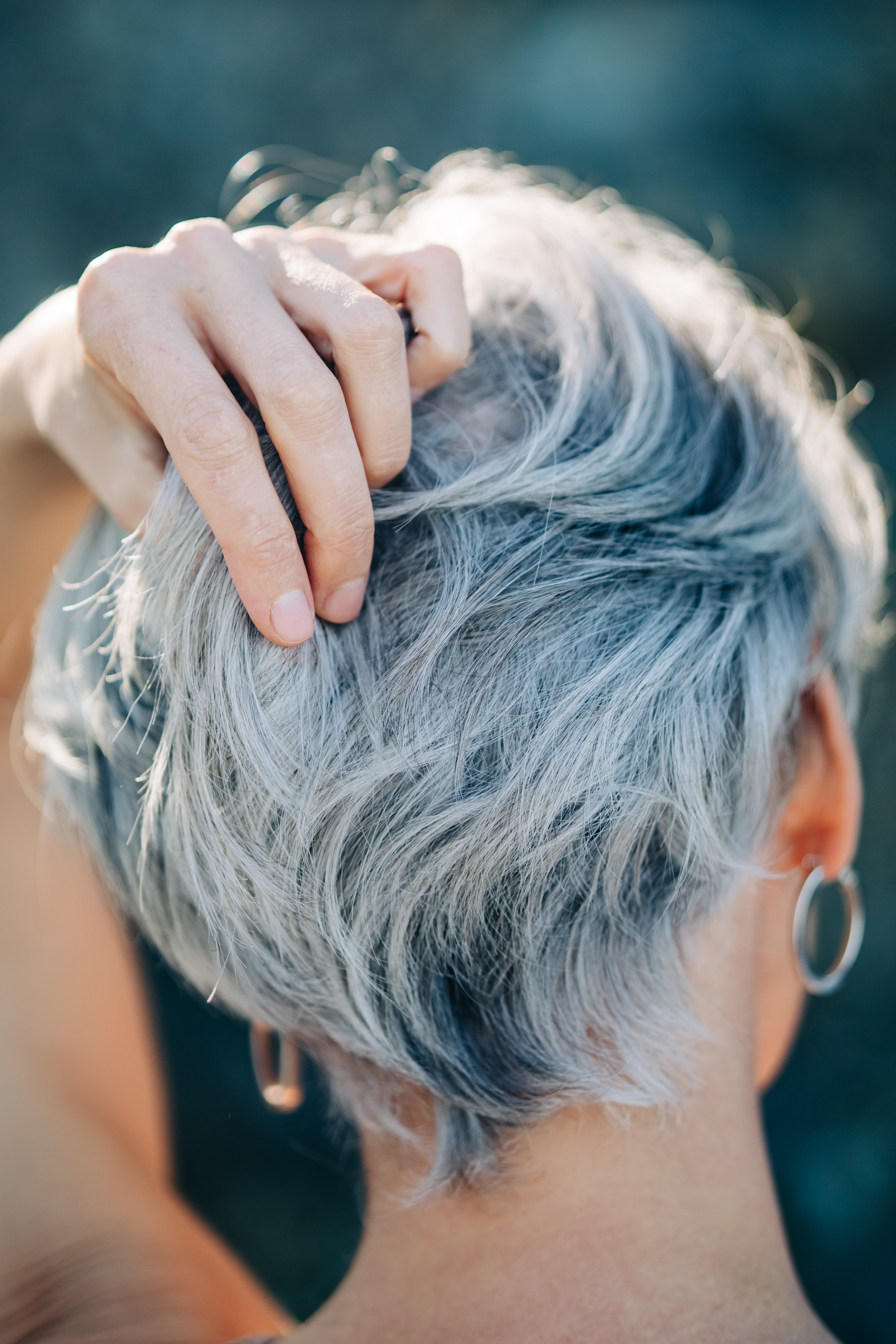A person with short silver hair, gently touching the back of their head