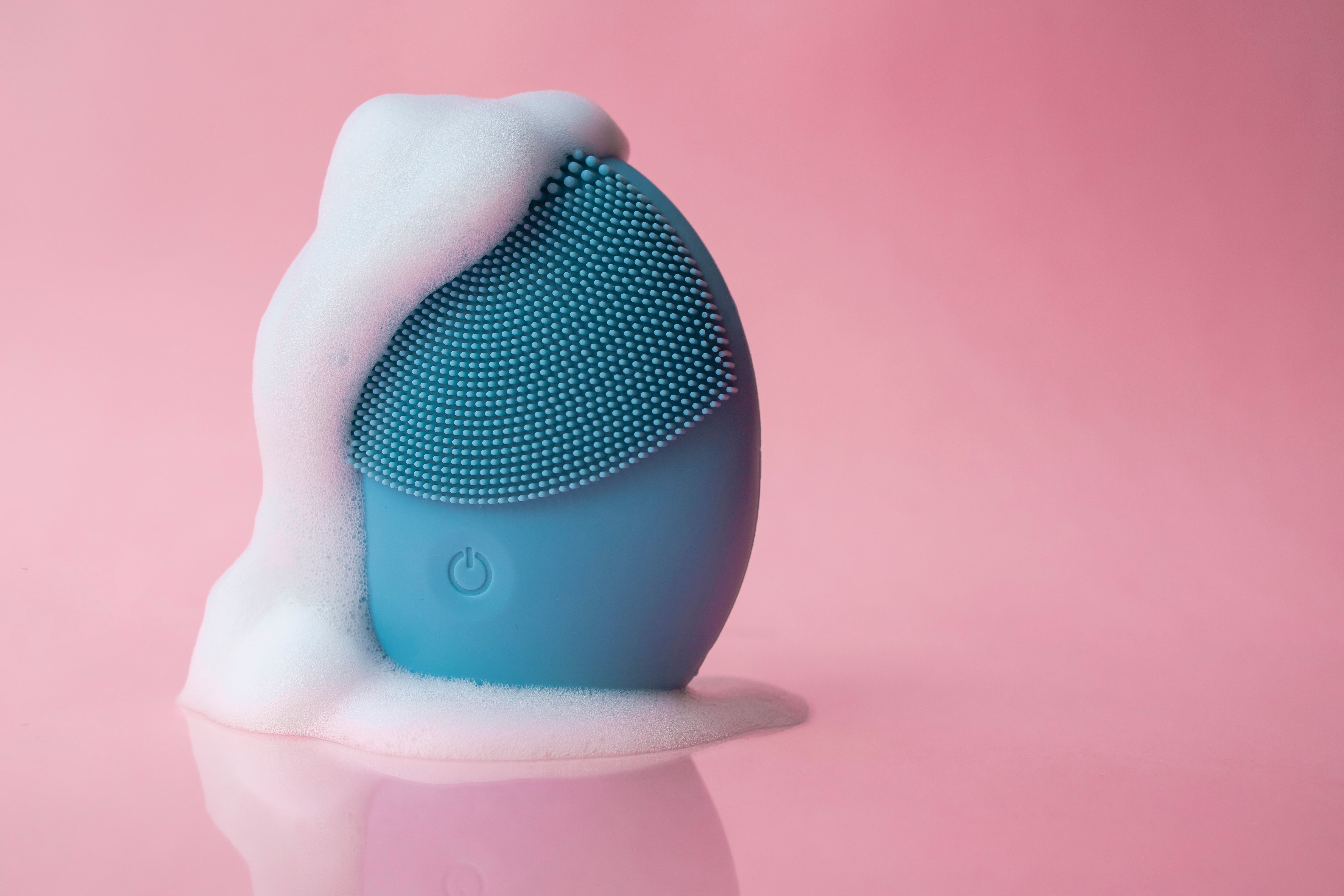 Facial cleansing device covered in foam against a plain background