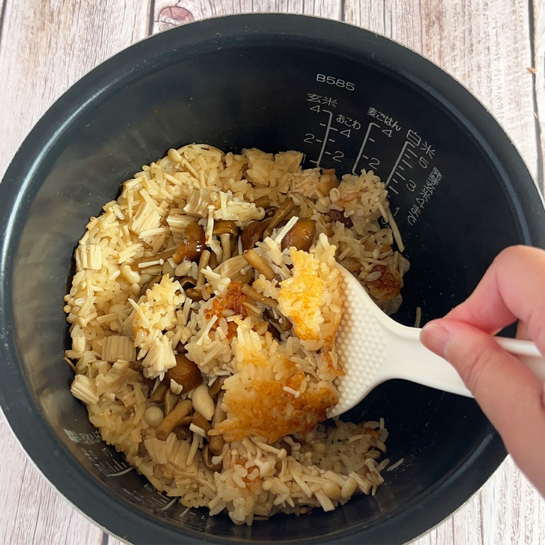 炊飯器に炊き立てのきのこご飯をしゃもじでよそう手元。