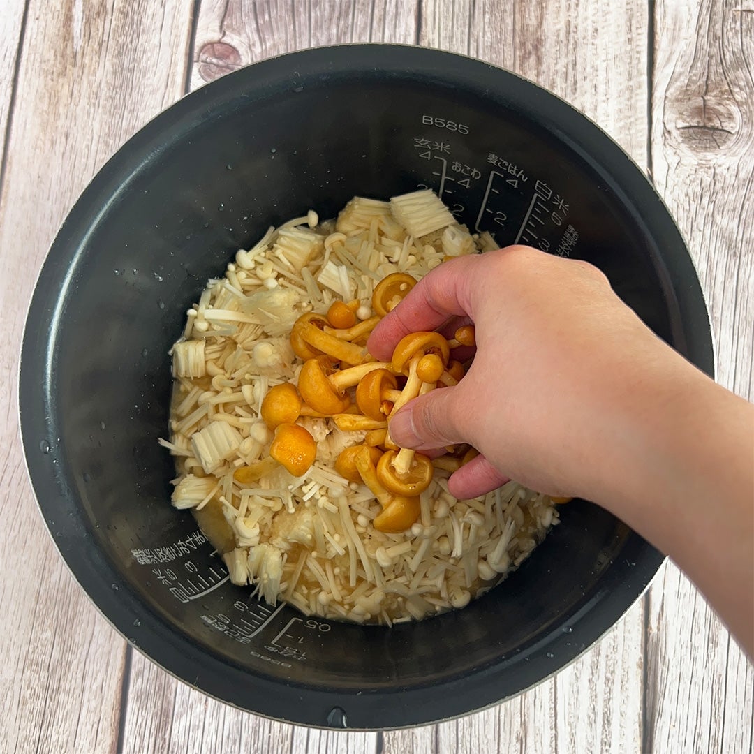 炊飯器の中できのこを調理する手。木製の背景。
