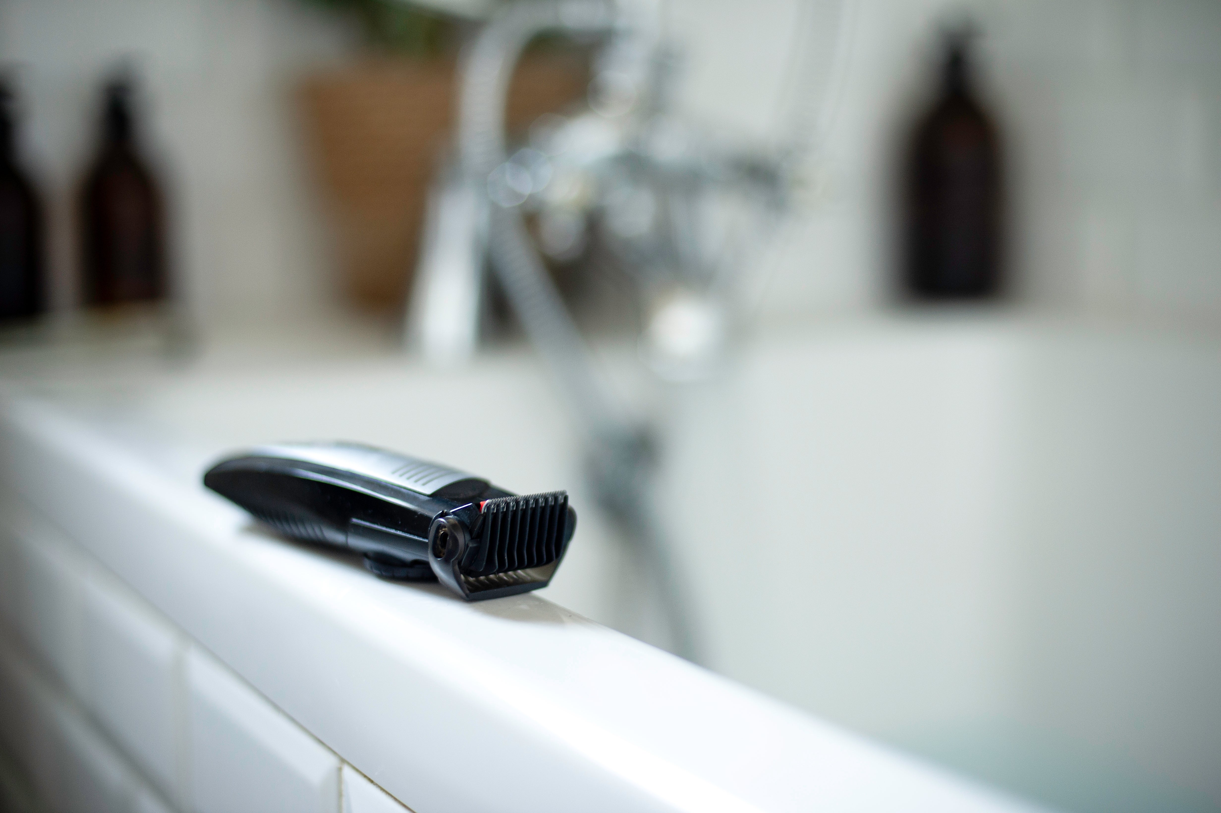 Electric hair trimmer resting on the edge of a bathtub
