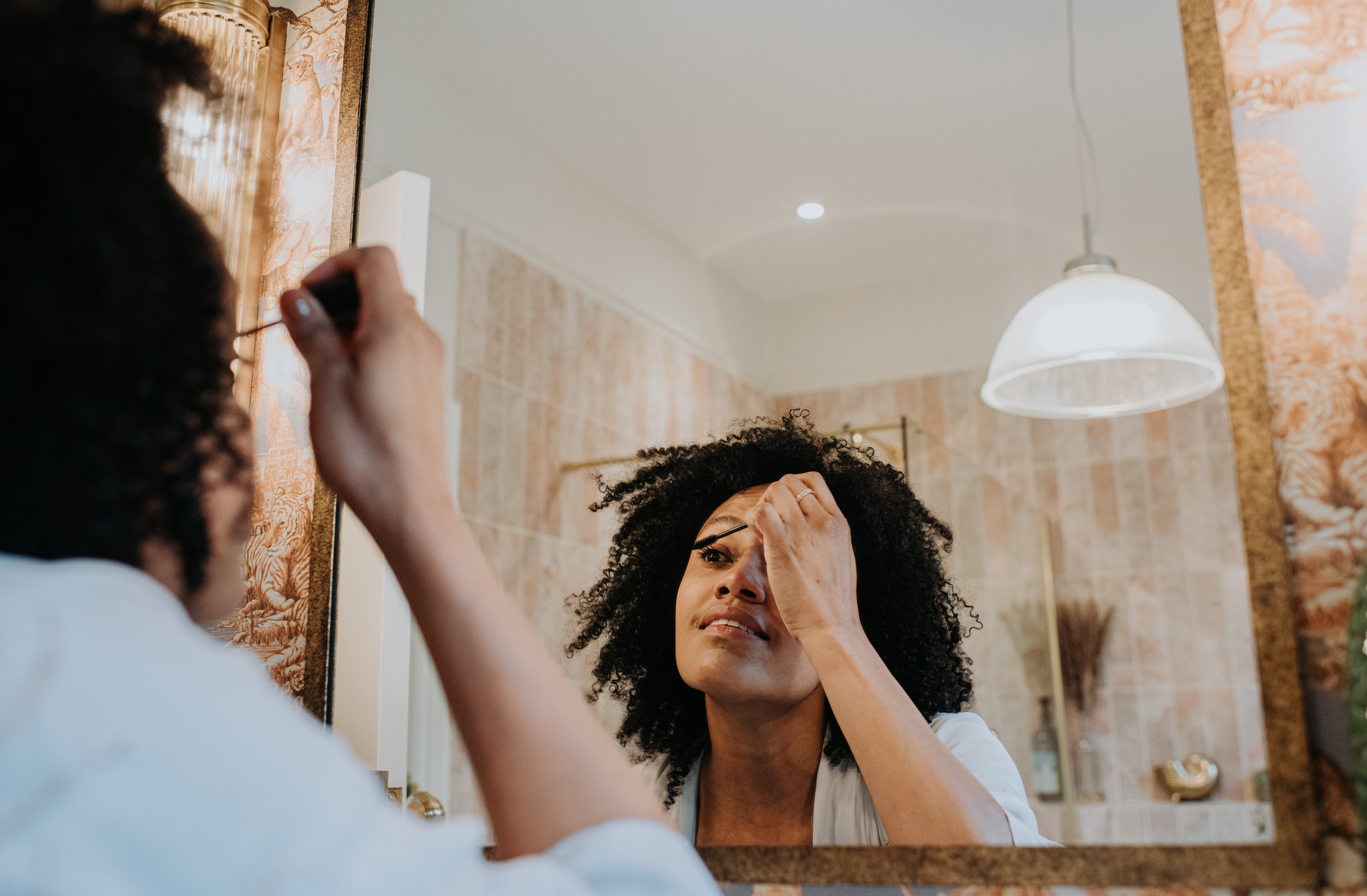 A person applying makeup in front of a mirror in a bathroom