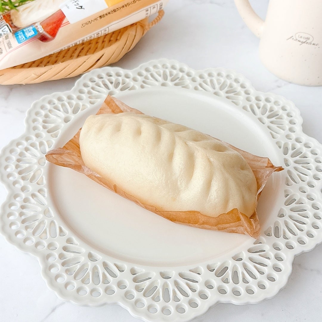 ミニストップの「餃子ドッグ」をお皿に乗せている。後ろにはパンのパッケージとカップが見える。