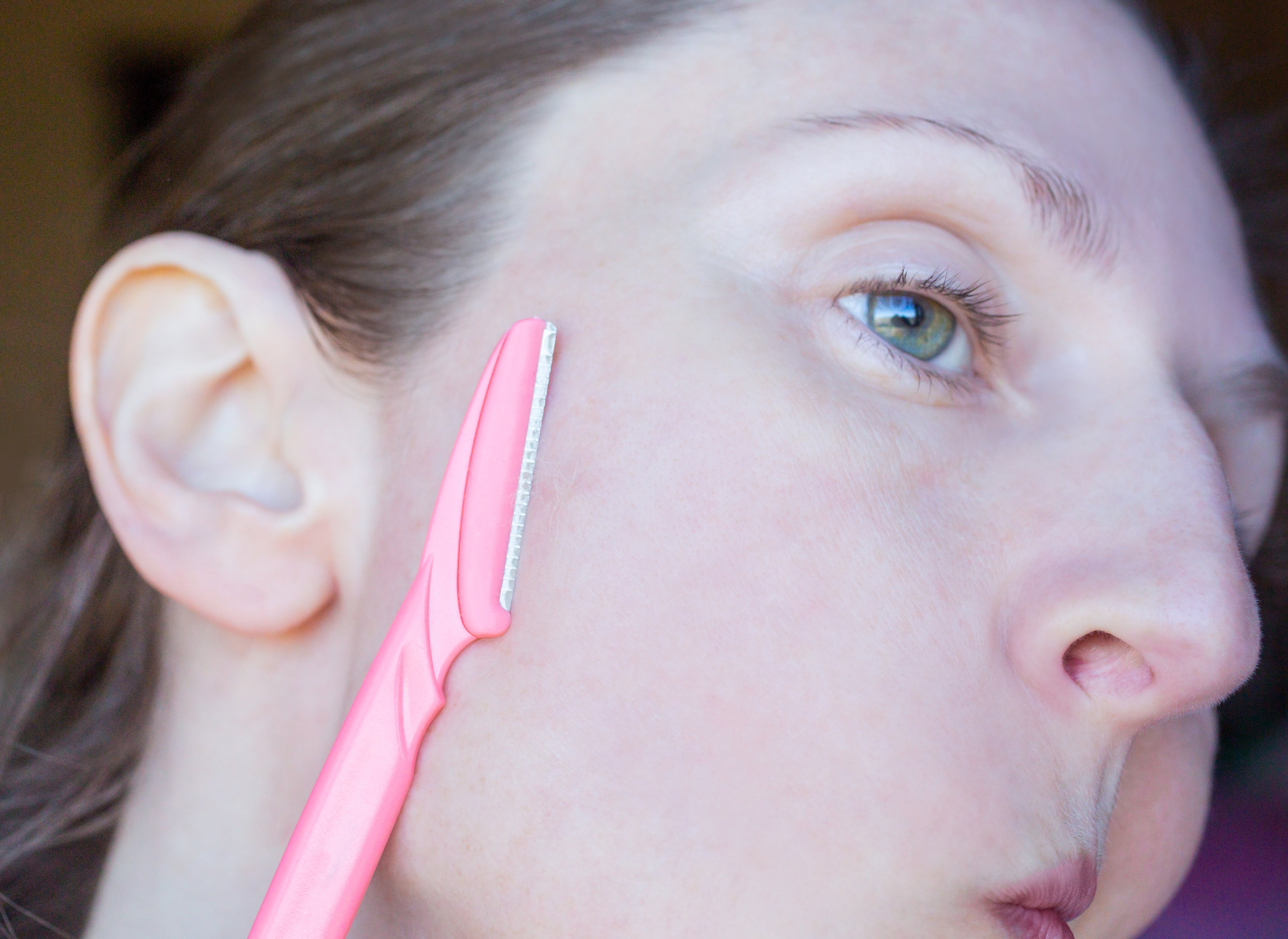 A person using a facial razor on their cheek