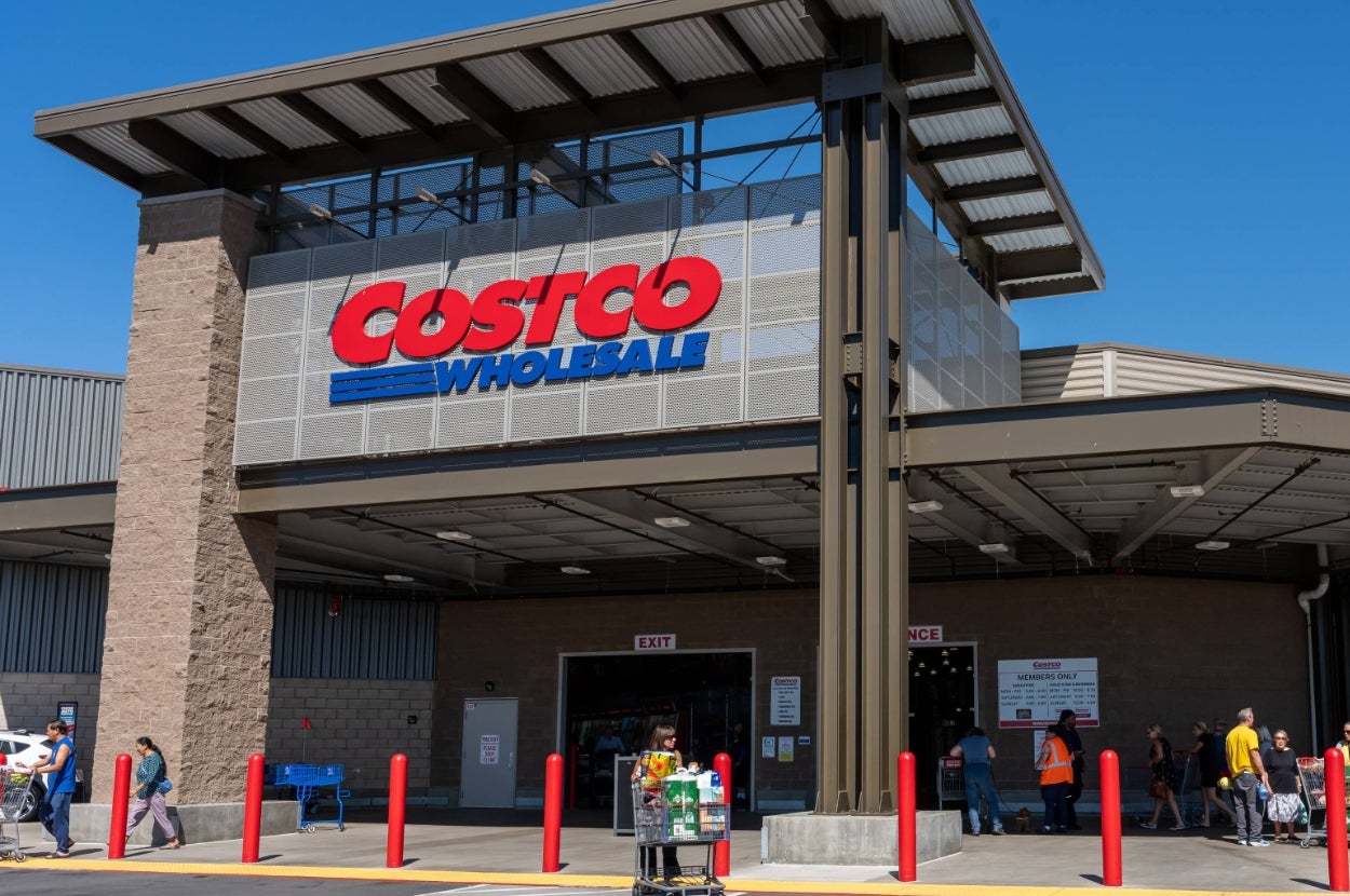 Costco Wholesale entrance with people entering and exiting, carts nearby, set in a busy retail environment