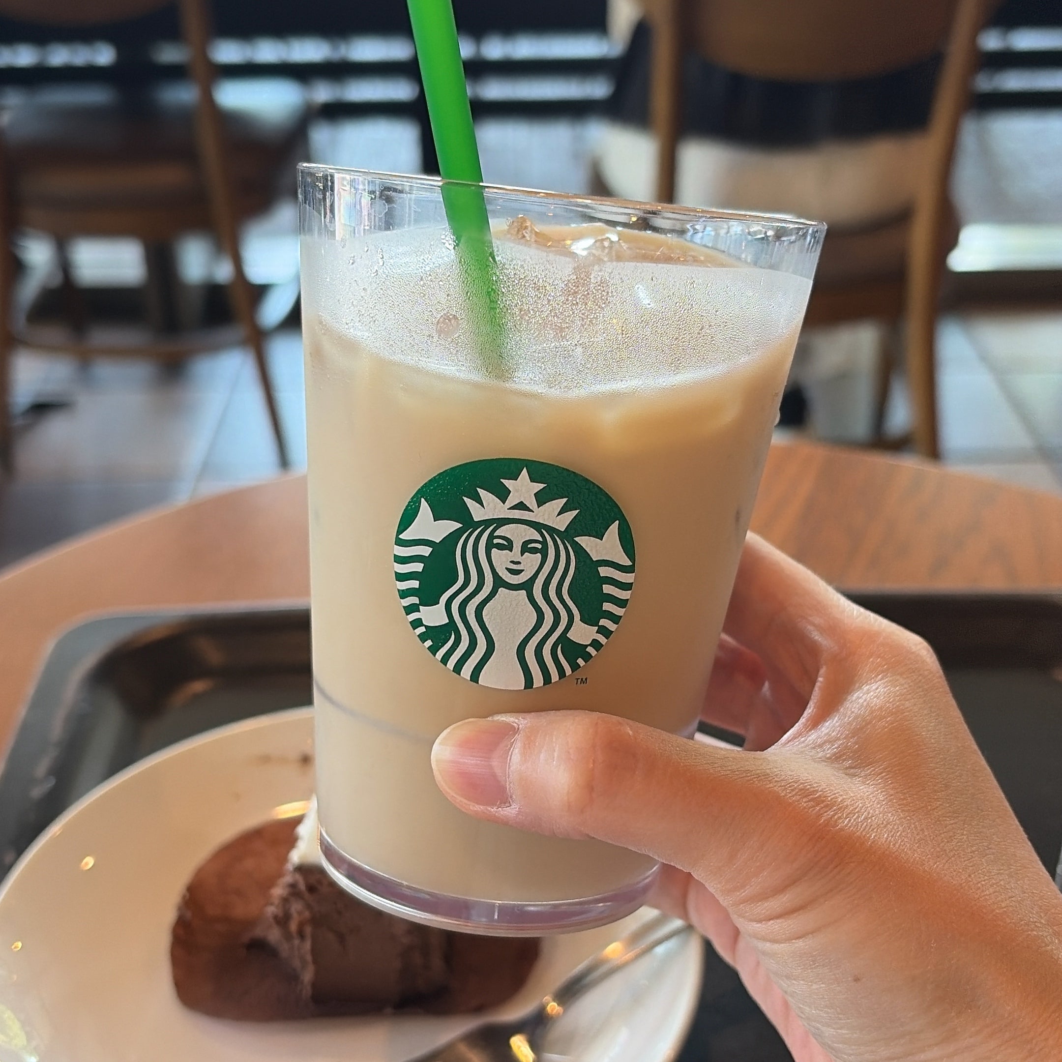 スタバ「チョコレートテリーヌ」カフェでアイスコーヒーを手に持つ様子。背景にチョコレートケーキの皿。