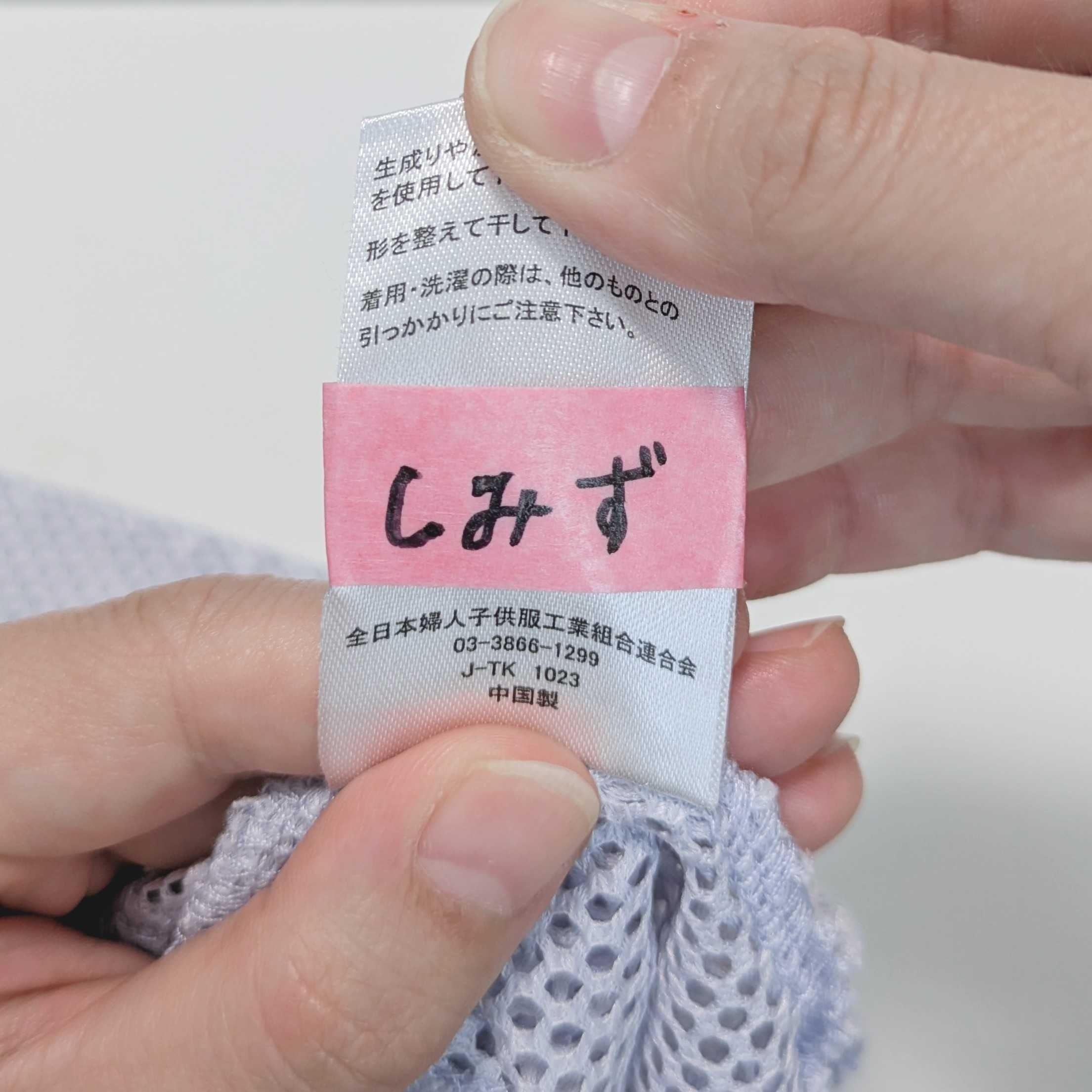 タグが縫い付けられた洋服を持つ手。タグには「しみず」と書かれています。