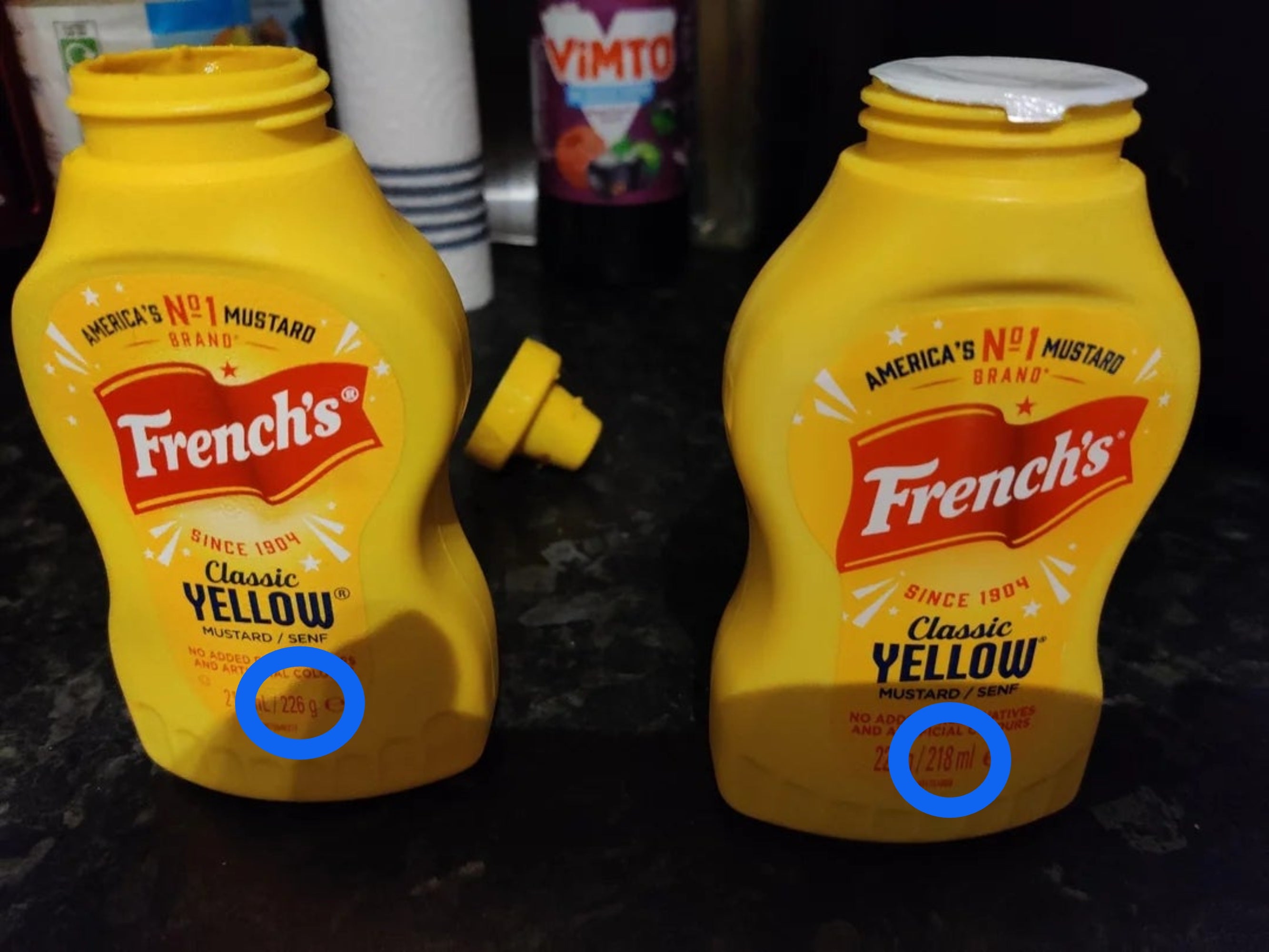 Two French's mustard bottles, 1  upright and 1  with its headdress  off, connected  a room  counter. A Vimto beverage vessel  is successful  the background
