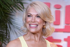 A person in a stylish sleeveless outfit smiles at a celebrity event, with a backdrop of greenery and large text