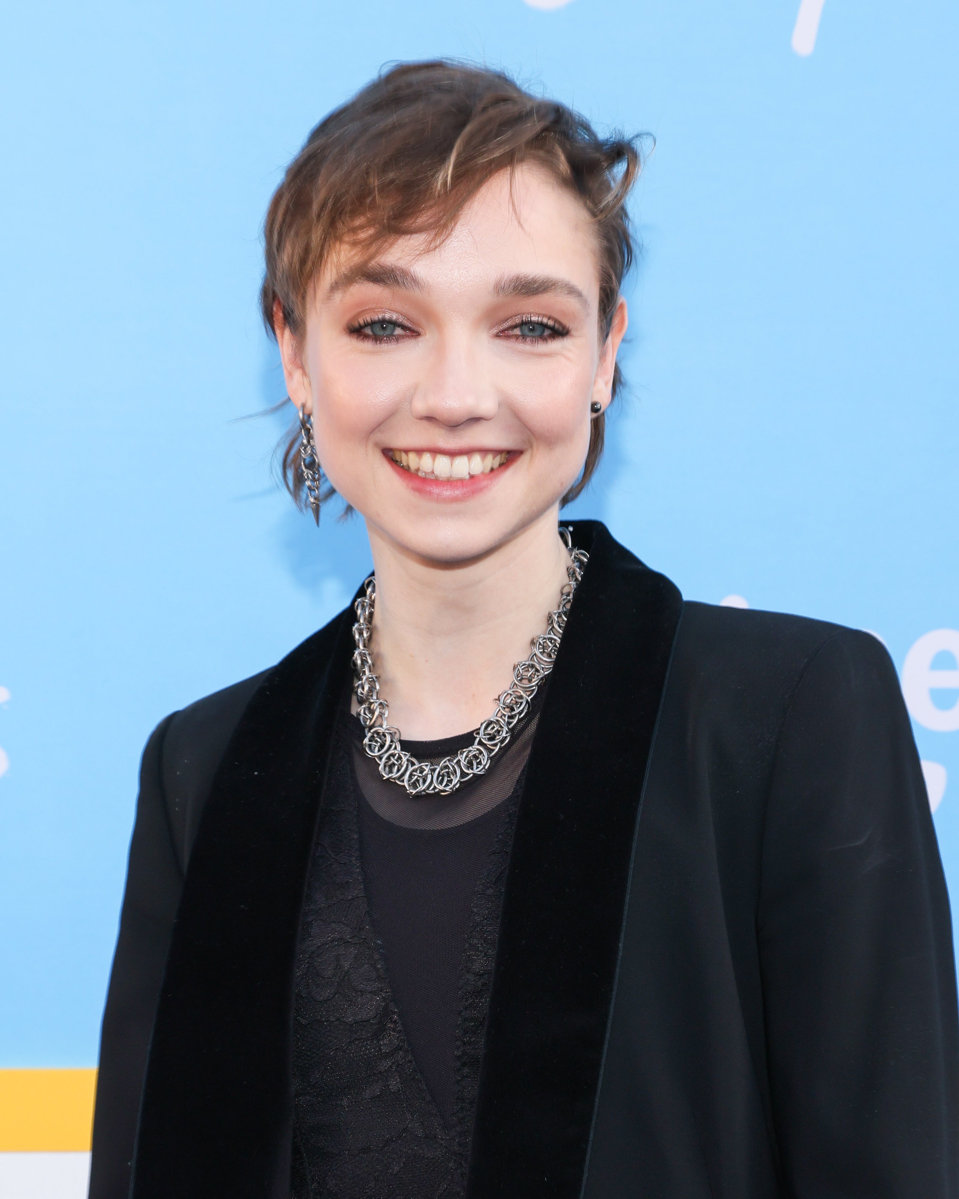 Person in a tailored suit with a velvet lapel and statement necklace, smiling at an event