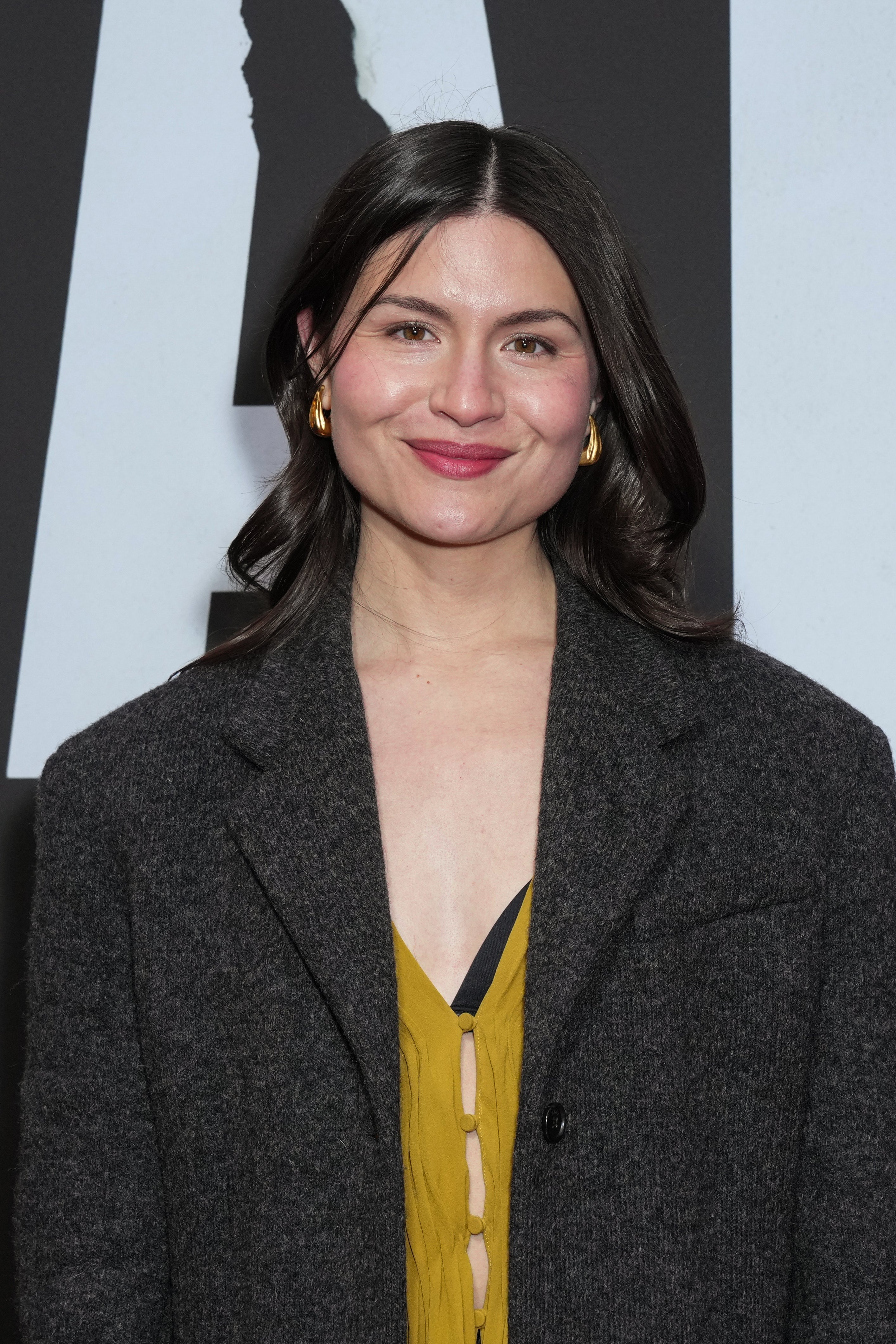 Person wearing a stylish open coat over a top with a deep neckline, posing at an event, smiling warmly at the camera