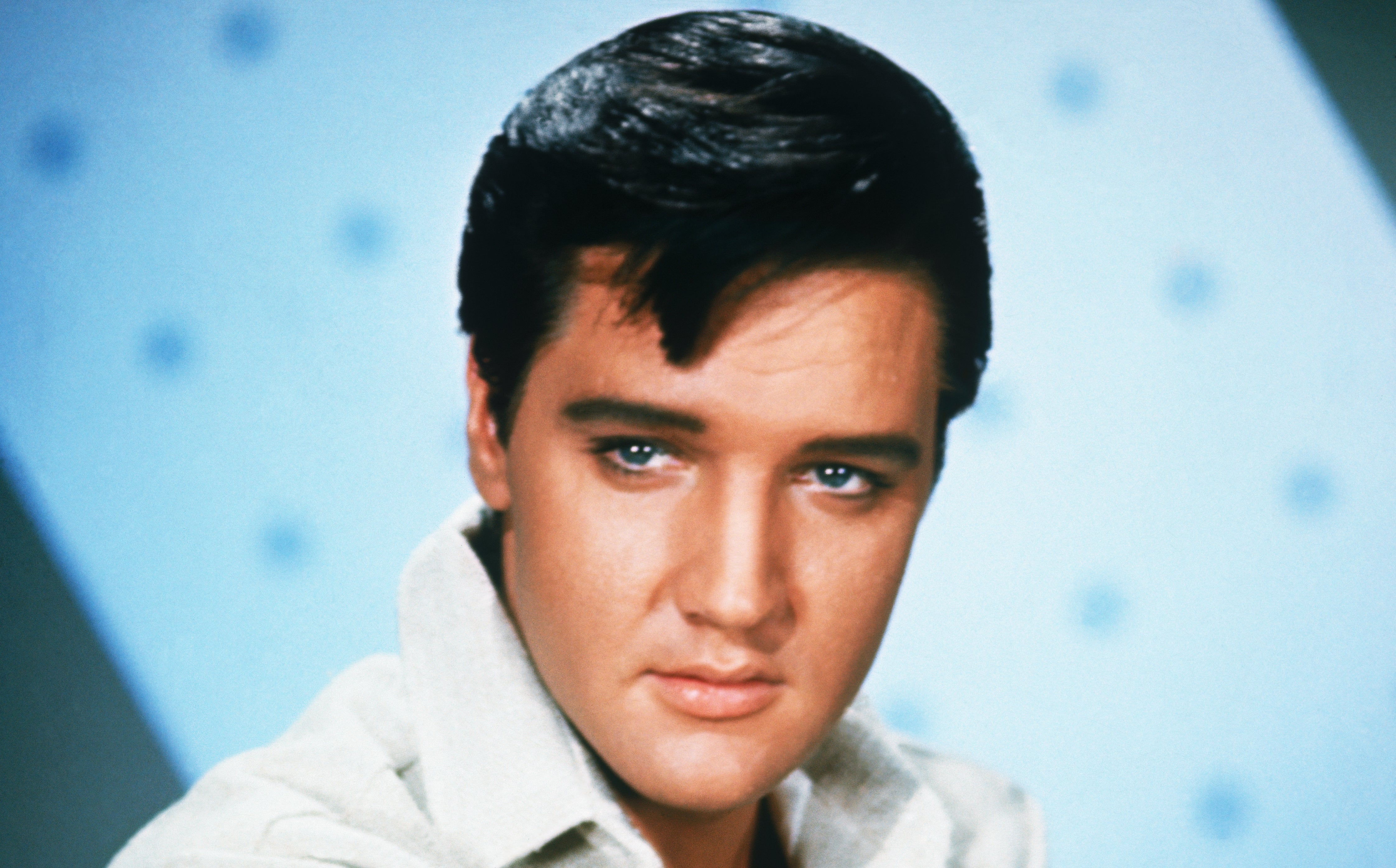 A person with styled dark hair and a collared shirt, looking slightly to the side, in a studio setting