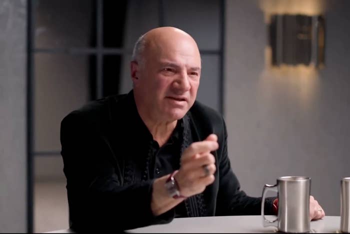 Man sitting at a table, gesturing while speaking, with a stainless steel mug in front of him