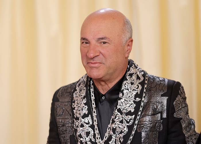 Person in an ornate embroidered jacket with intricate silver patterns, smiling at an event