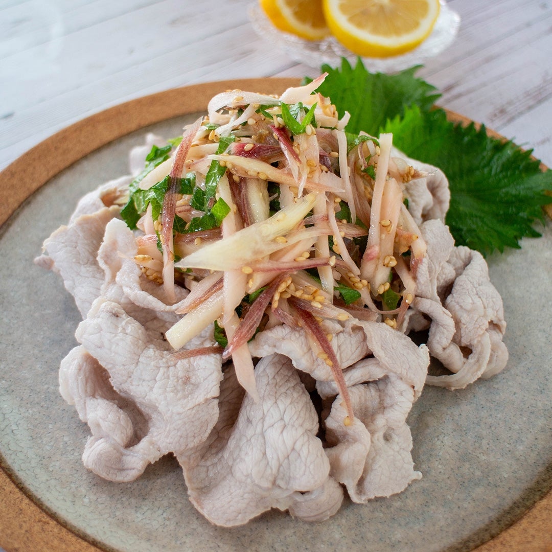 冷しゃぶサラダのイメージ。薄切り豚肉と野菜の盛り合わせが皿に美しく盛られ、後ろにはレモンのスライスが添えられている。
