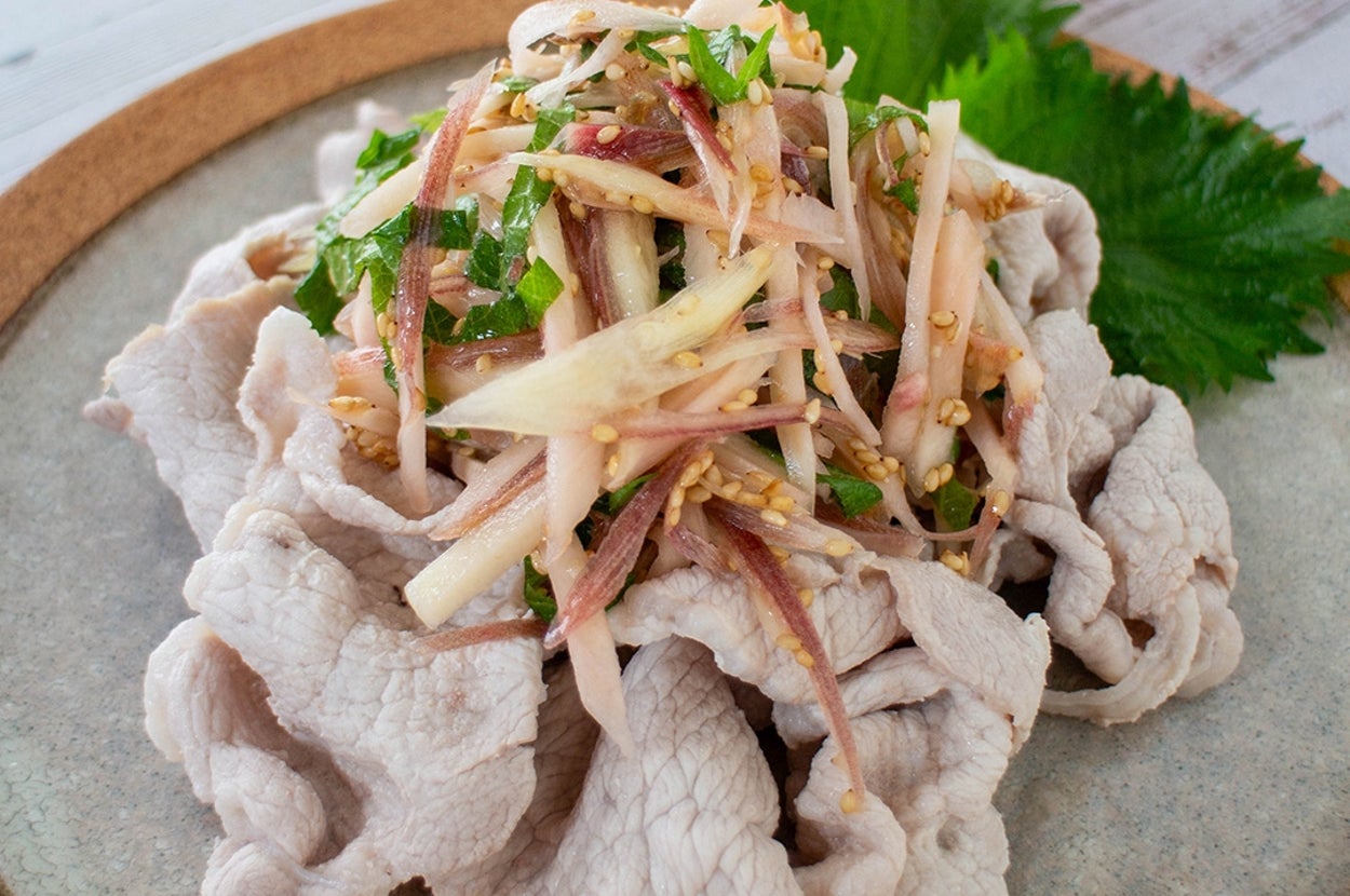 冷しゃぶサラダのイメージ。薄切り豚肉と野菜の盛り合わせが皿に美しく盛られ、後ろにはレモンのスライスが添えられている。