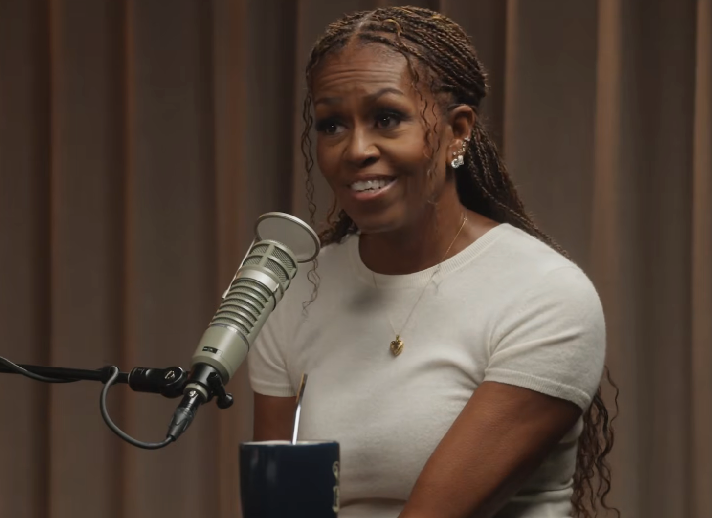 A idiosyncratic with braided hairsbreadth smiles portion speaking into a microphone, perchance during a podcast oregon interview