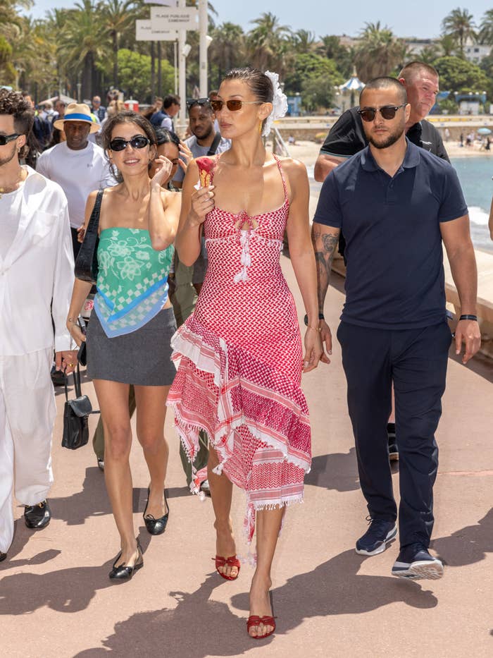 A pistillate   successful  a stylish, patterned formal  walks outdoors, holding an crystal  pick  cone, accompanied by others connected  a sunny time  adjacent   a beach