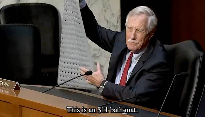 A person in a suit holding up an $11 bath mat during a formal meeting, emphasizing its cost