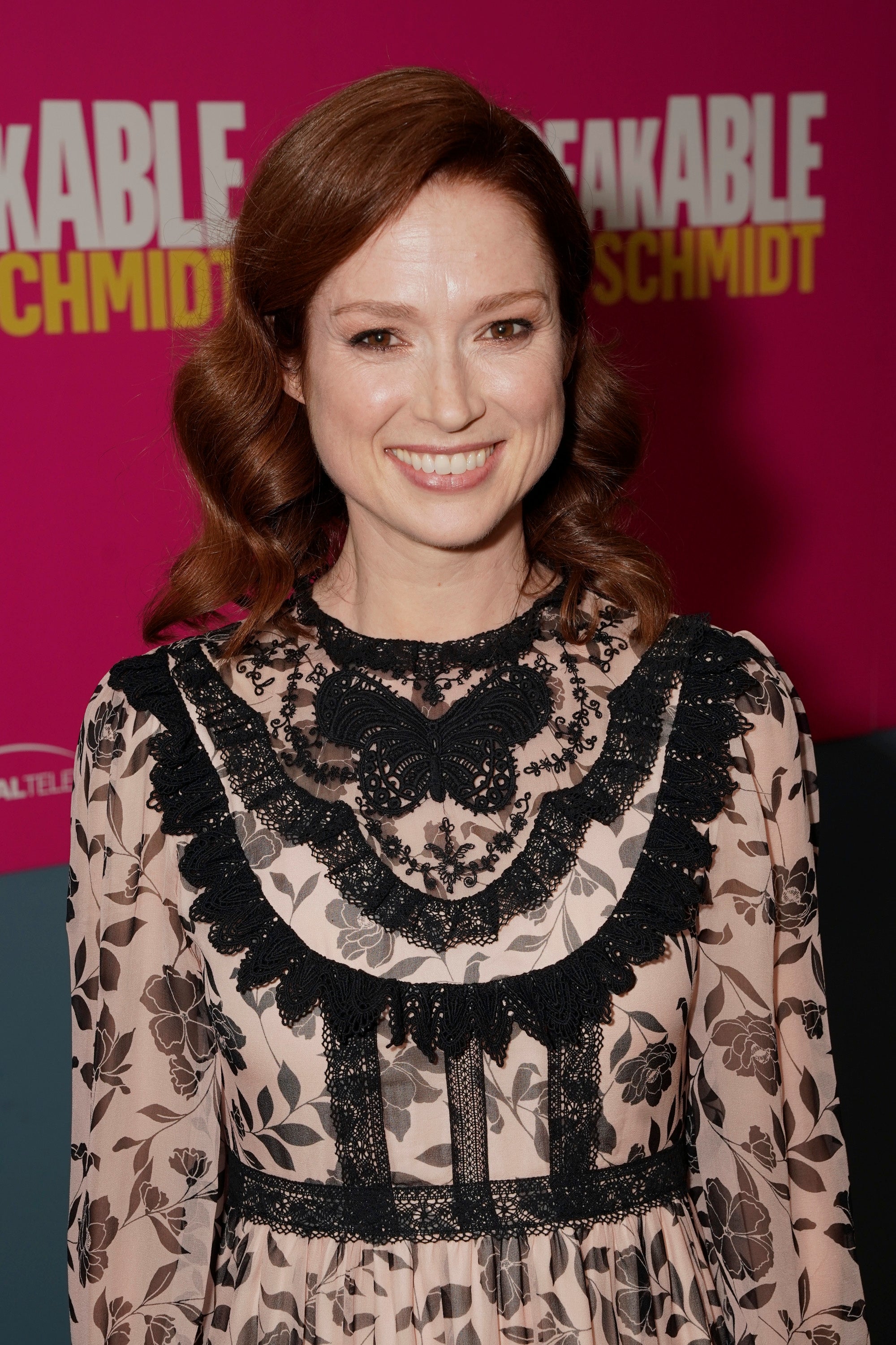 Ellie Kemper smiling astatine a reddish carpet lawsuit with an "Unbreakable Kimmy Schmidt" backdrop