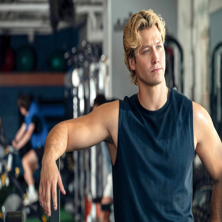 Person in a sleeveless shirt stands in a gym with exercise equipment in the background