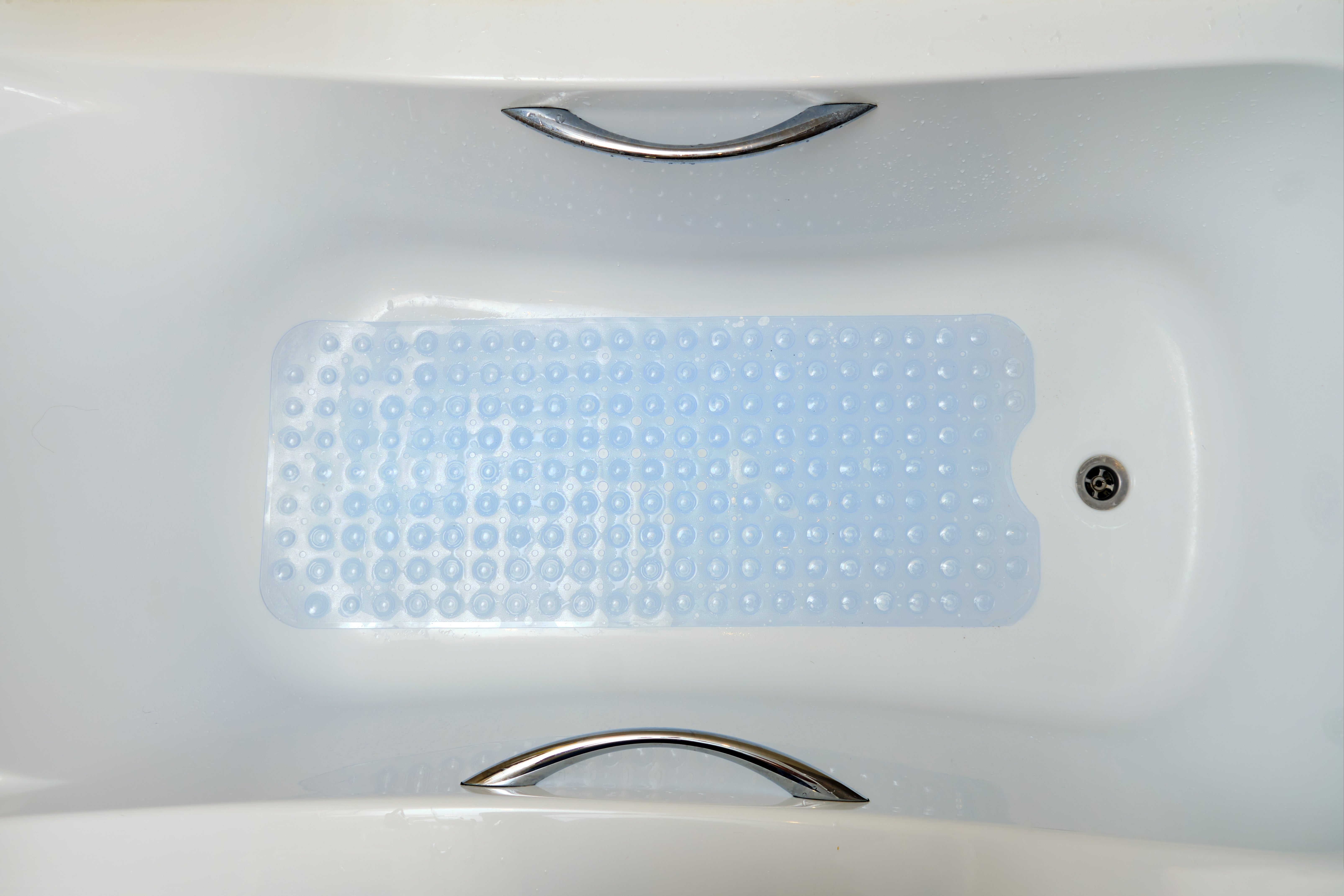 Bathtub with silver handles and a textured bath mat to prevent slipping
