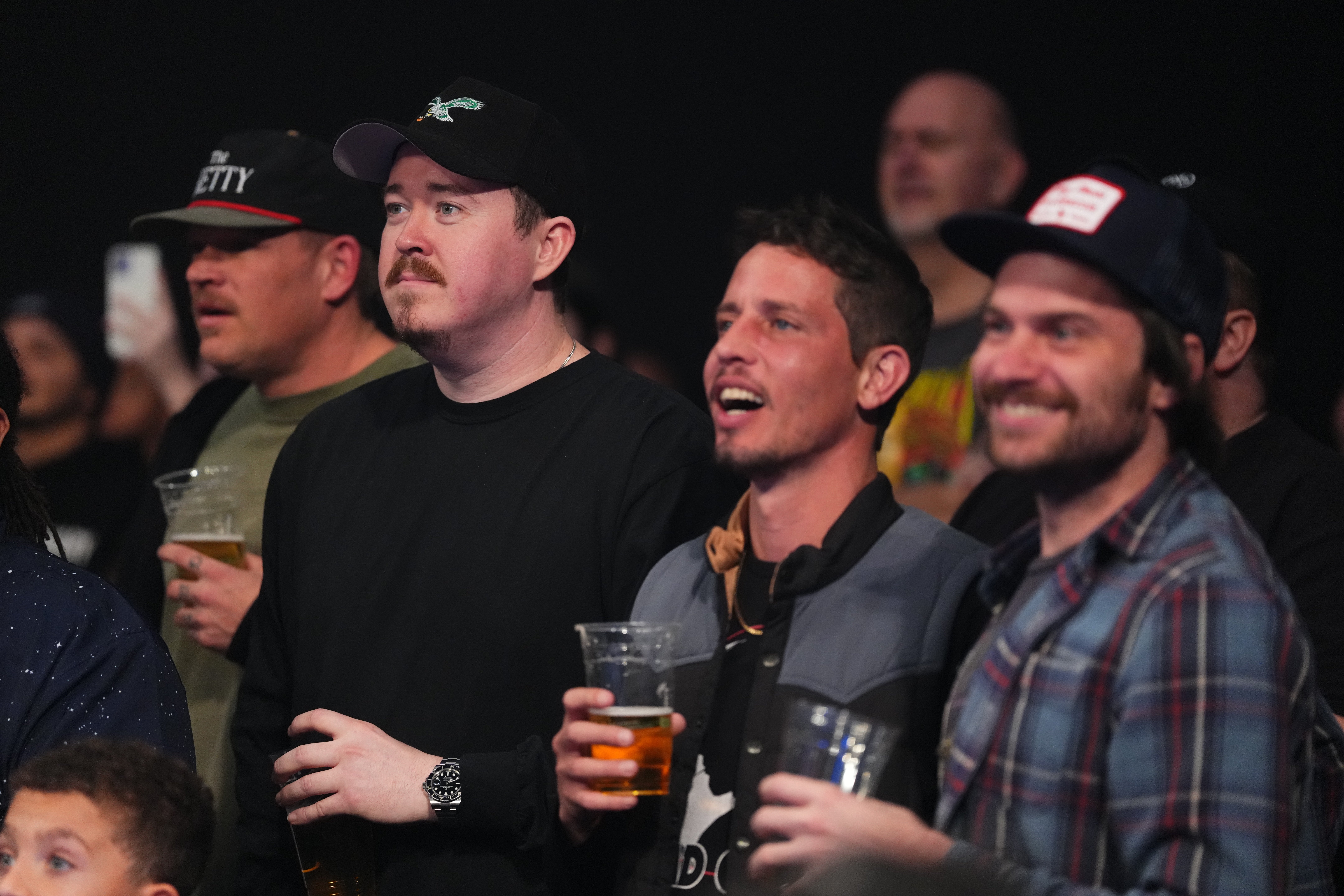 Several men basal successful a crowd, holding drinks and watching an lawsuit with expressions of excitement and interest