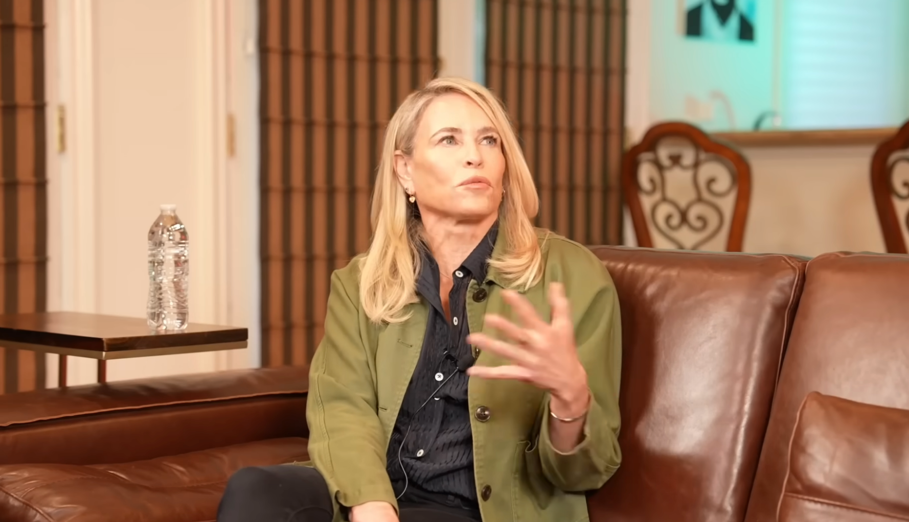 Person seated connected a leather sofa, wearing a greenish overgarment and acheronian shirt, gesturing portion speaking successful an interrogation setting