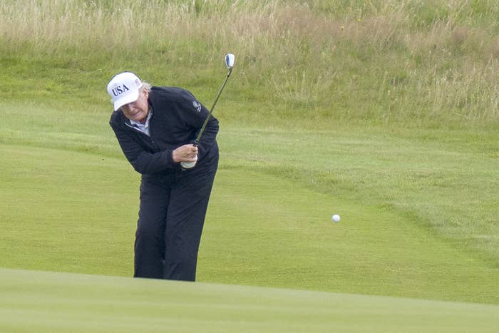 Person playing golf, wearing a headdress  labeled "USA," swinging a nine  connected  a grassy course
