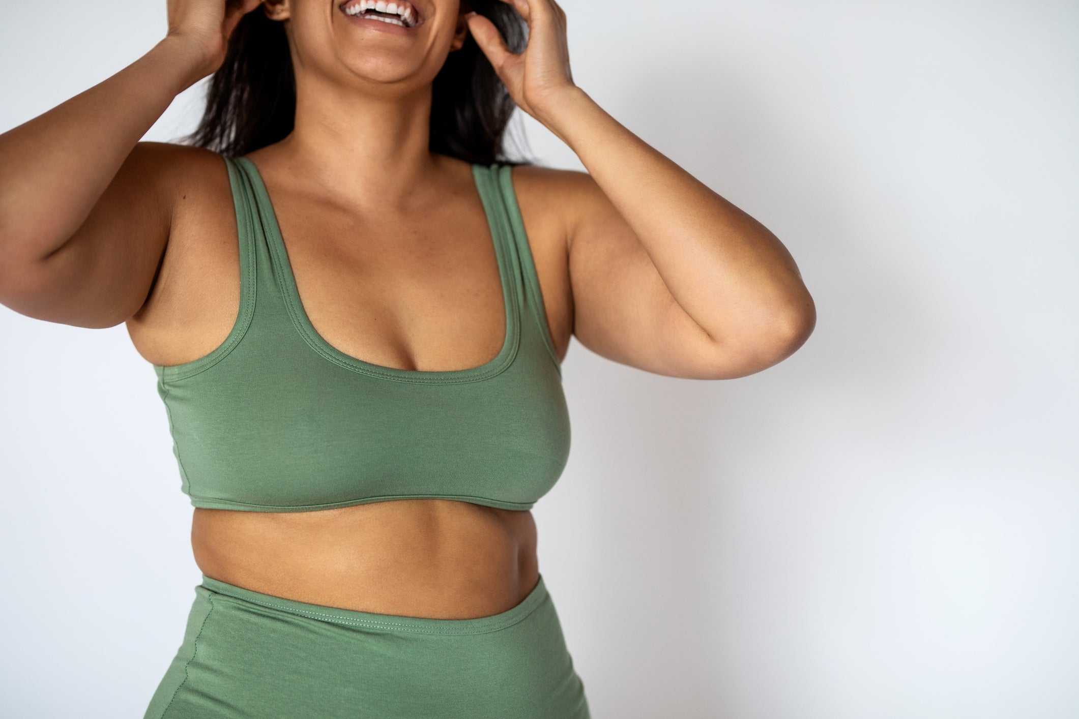 Person in fitness wear smiling, adjusting hair. Image suggests positivity and health-related content