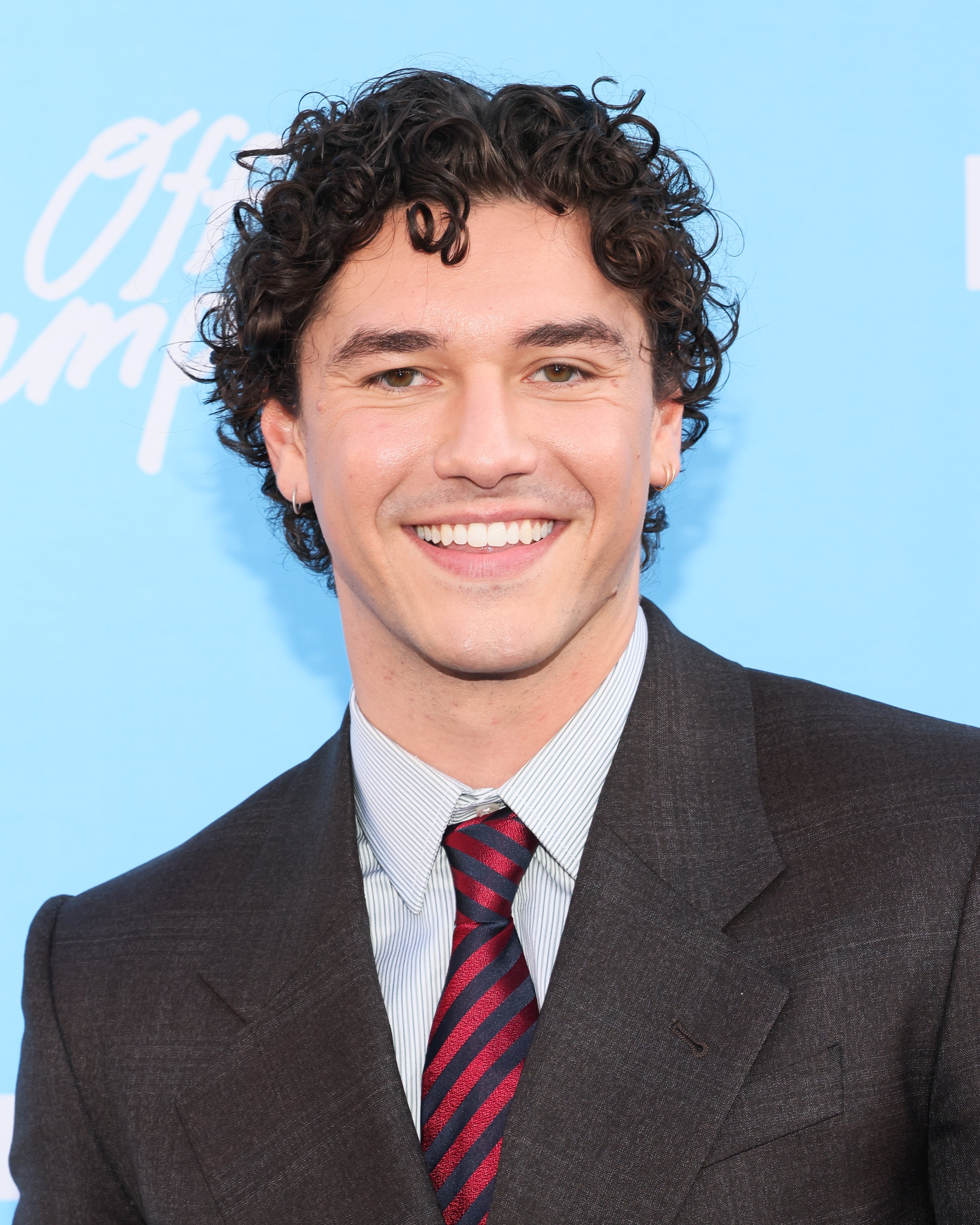 Person smiling in a formal dark suit with a striped tie, against a blue backdrop