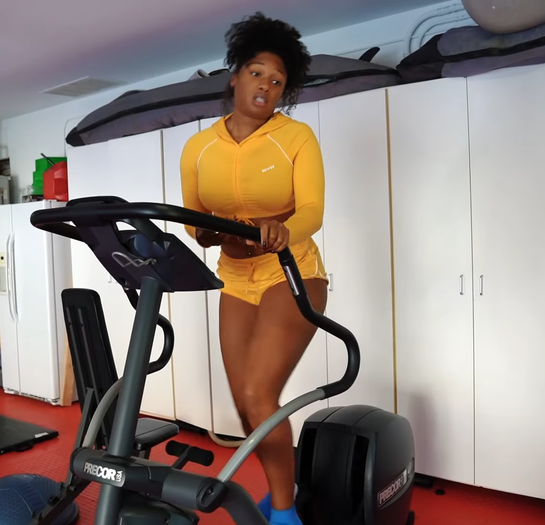 Person in athletic outfit using an exercise bike in a home gym with storage closets and workout equipment in the background