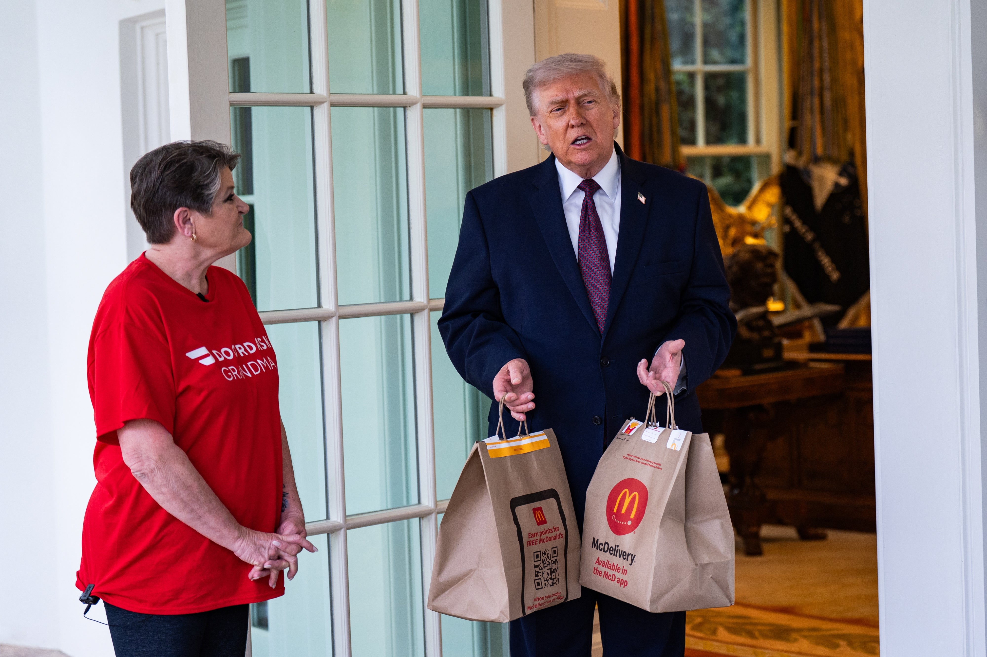 A person in a suit holds McDonald's bags beside a casually dressed individual, possibly discussing a delivery or business meeting