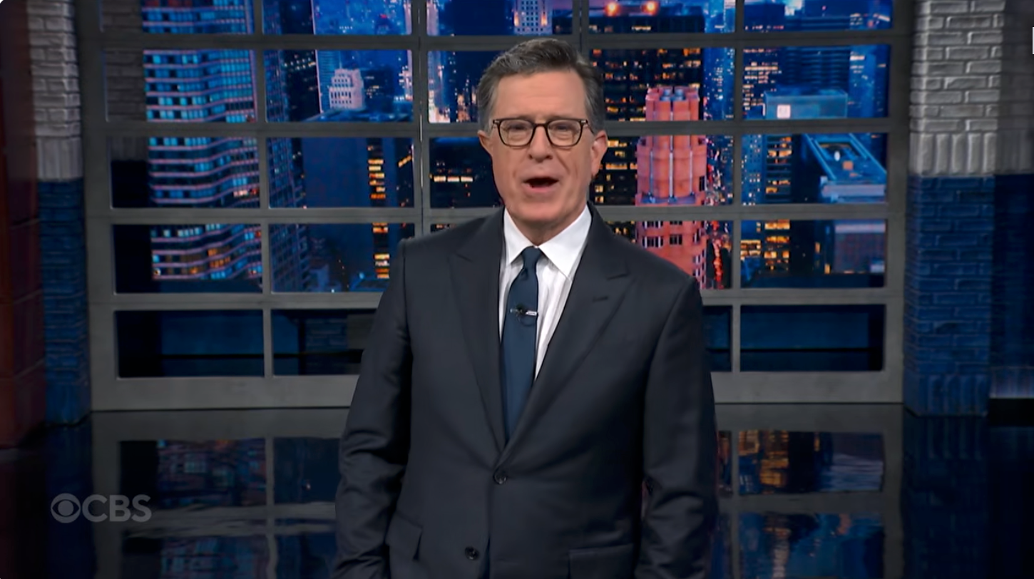 A person in a suit speaks animatedly in front of a cityscape backdrop during a TV show segment