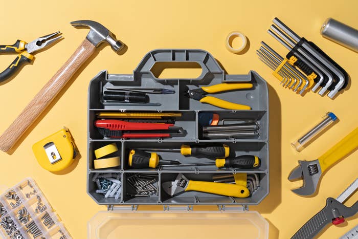 Toolbox with assorted tools including hammer, pliers, portion    measure, wrench, screwdrivers, and hex keys arranged connected  a surface
