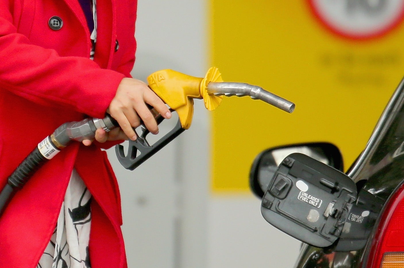 Person refueling car at gas station with yellow nozzle