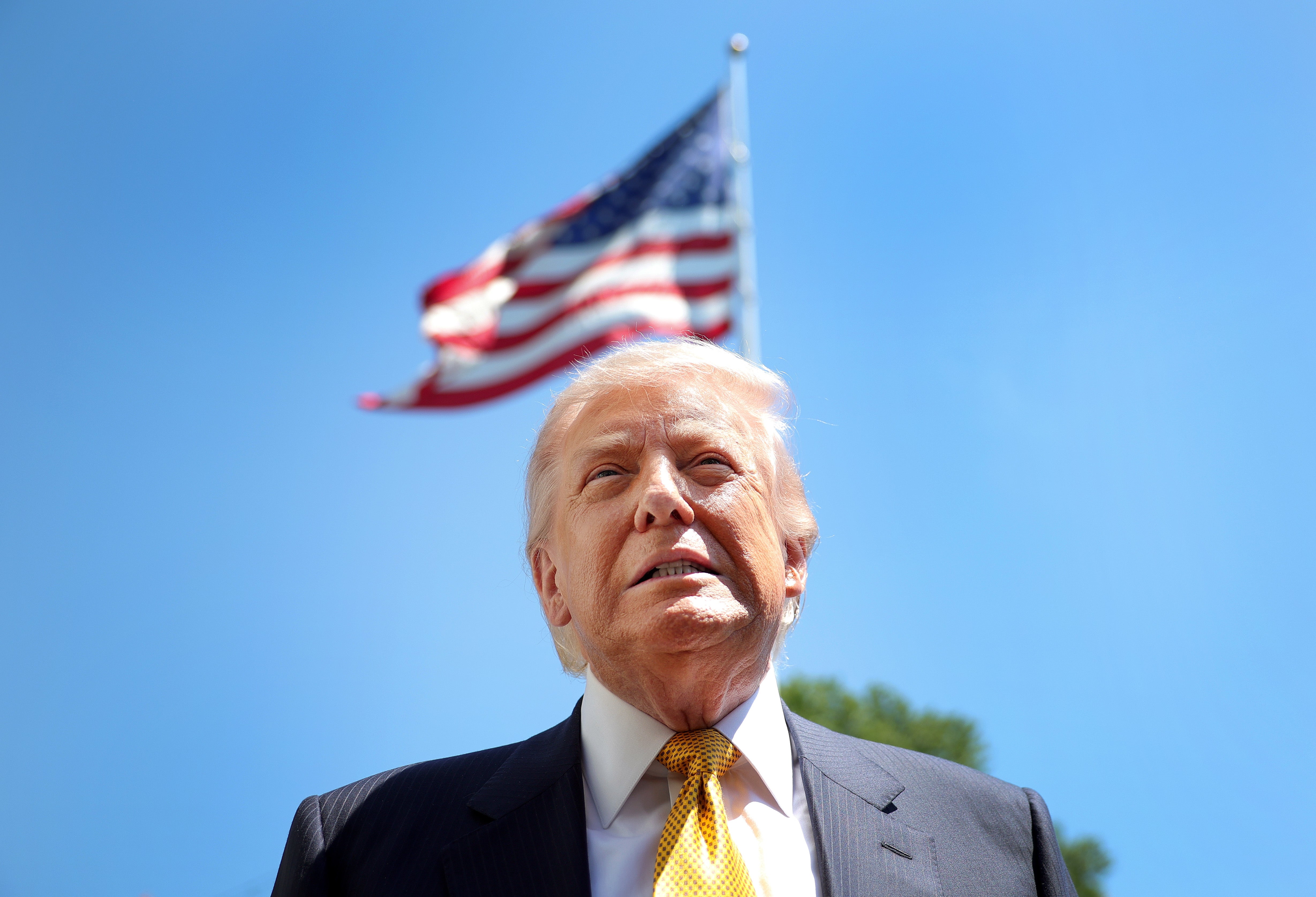 A person in a suit stands outdoors with an American flag waving in the background. The image suggests a connection to American work and leadership themes