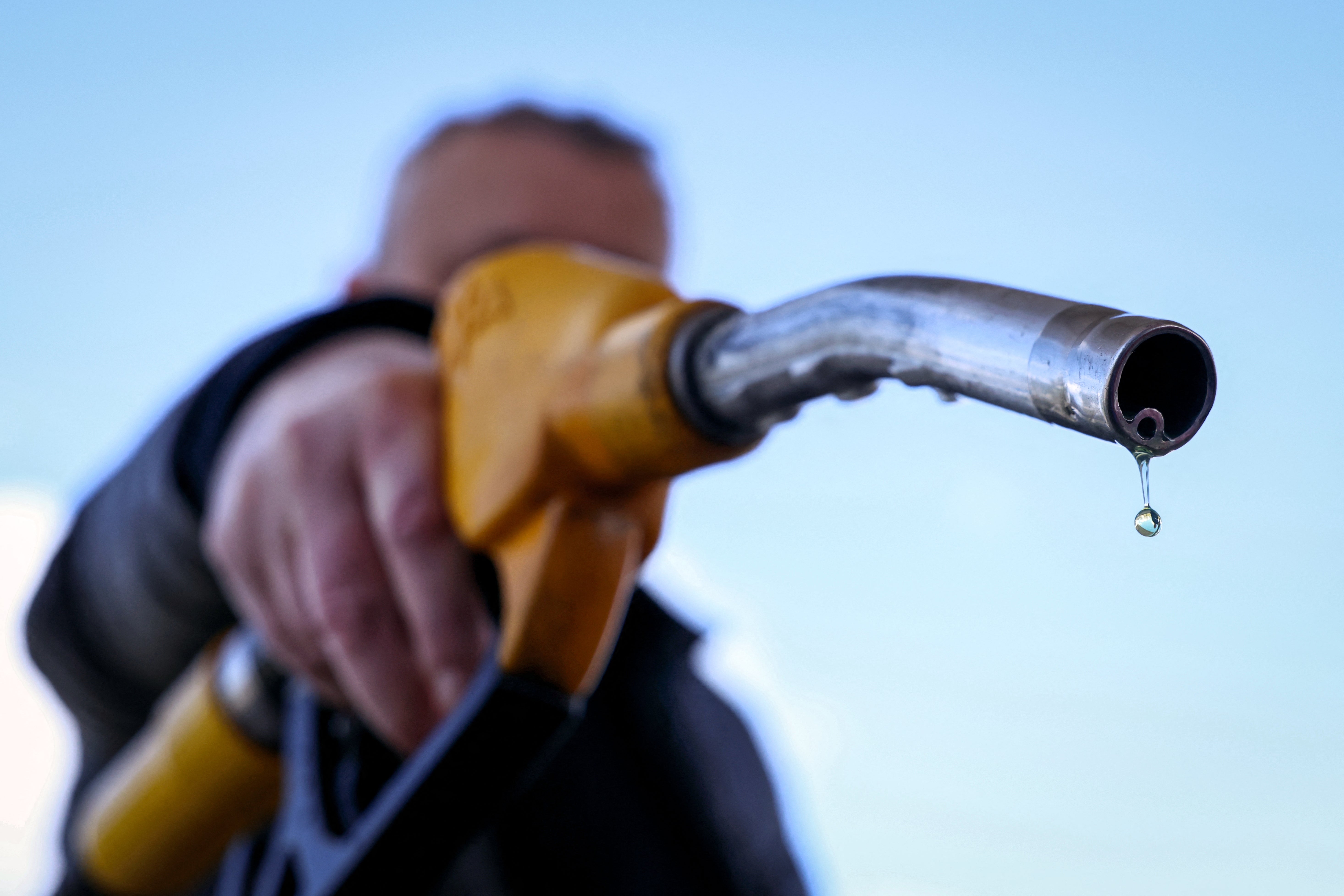 Person holding a fuel pump nozzle with a droplet at the tip, symbolizing fuel consumption and costs in a Work &amp;amp; Money context