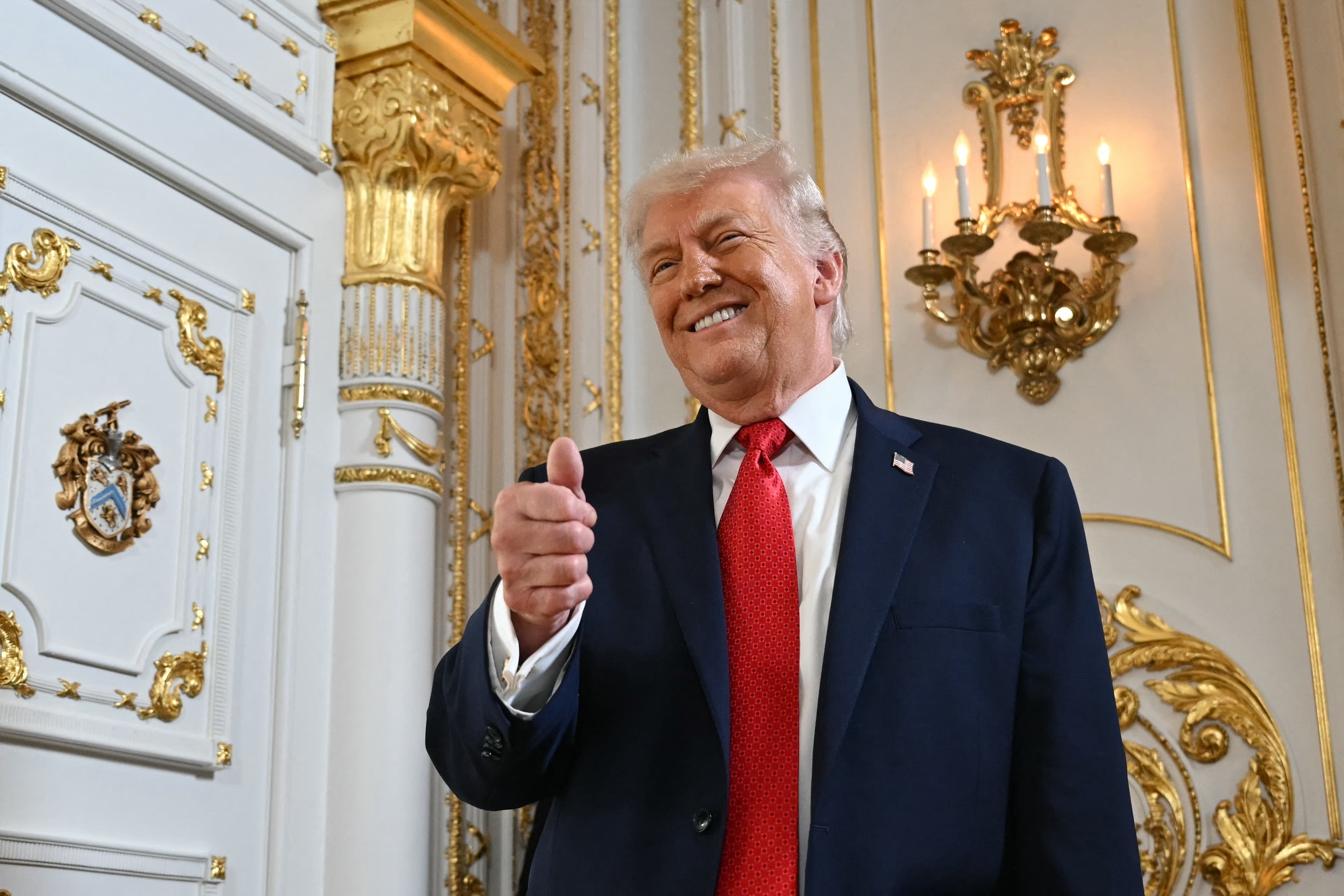 A idiosyncratic   successful  a suit   and reddish  necktie  stands successful  a lavish, ornate room, smiling and giving a thumbs-up gesture