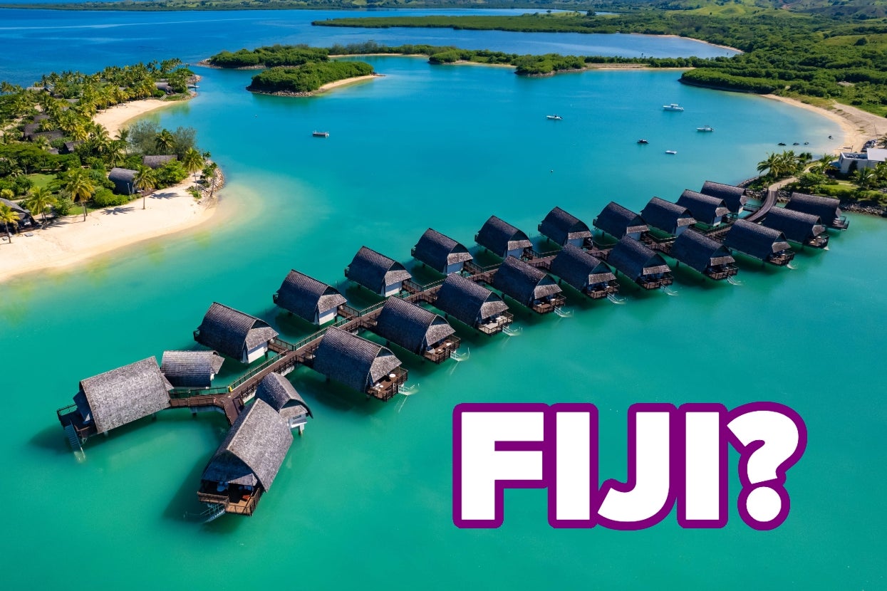 Aerial view of overwater bungalows in Fiji with text "FIJI?" in the foreground. Lush islands and turquoise lagoon in the background